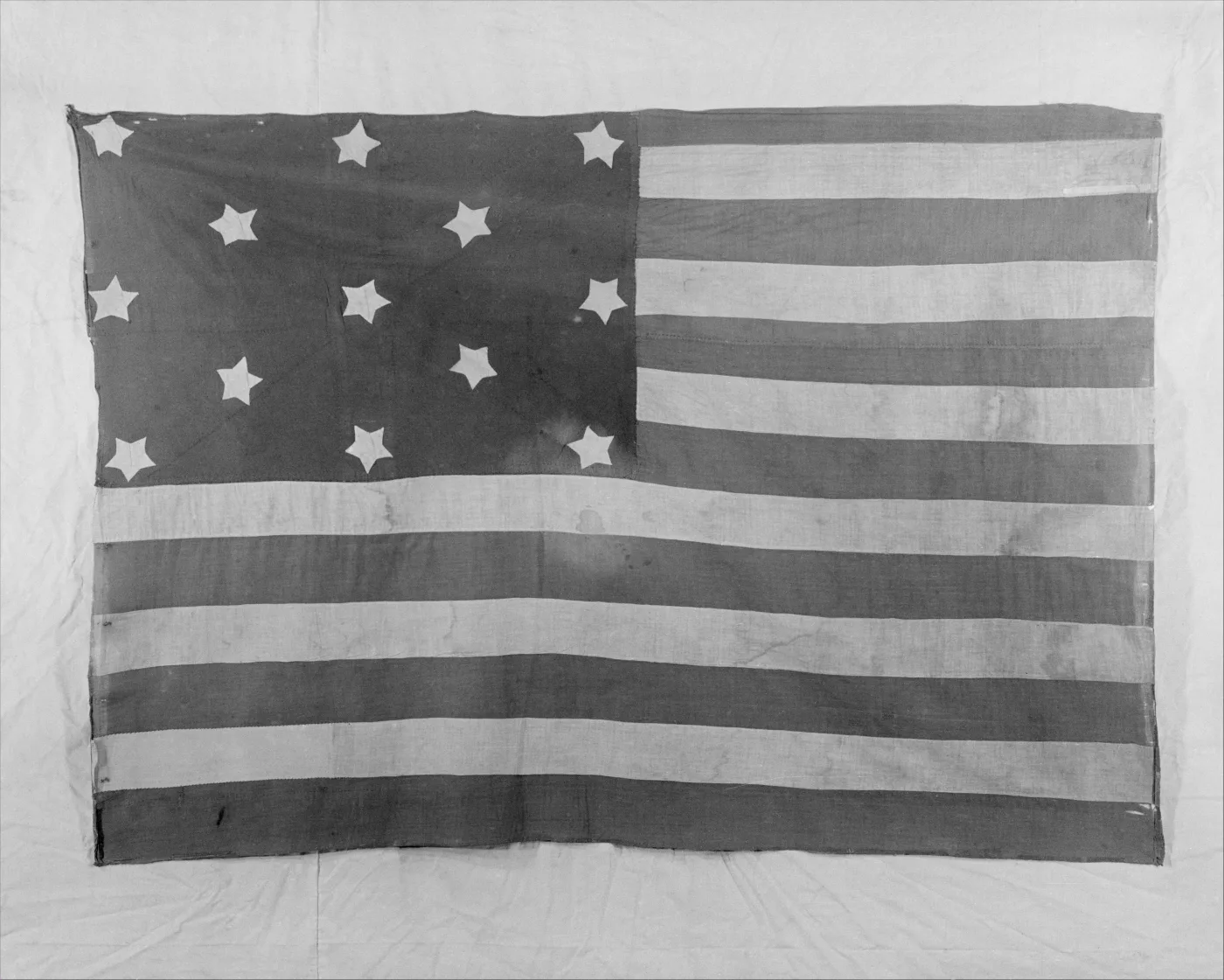 Hand-sewn flag with a dark canton bearing a scattered arrangement of white stars beside horizontal stripes, photographed flat against a pale ground