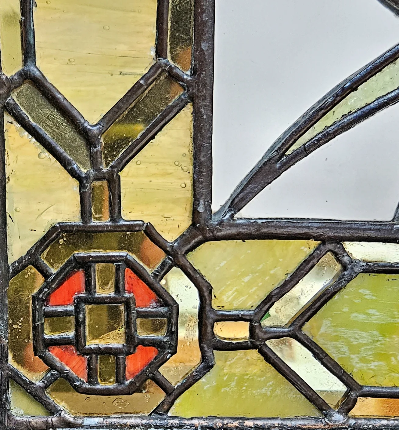 Close view of leaded glass showing the H-profile lead strips and the solder joints where they meet, with amber and red glass either side