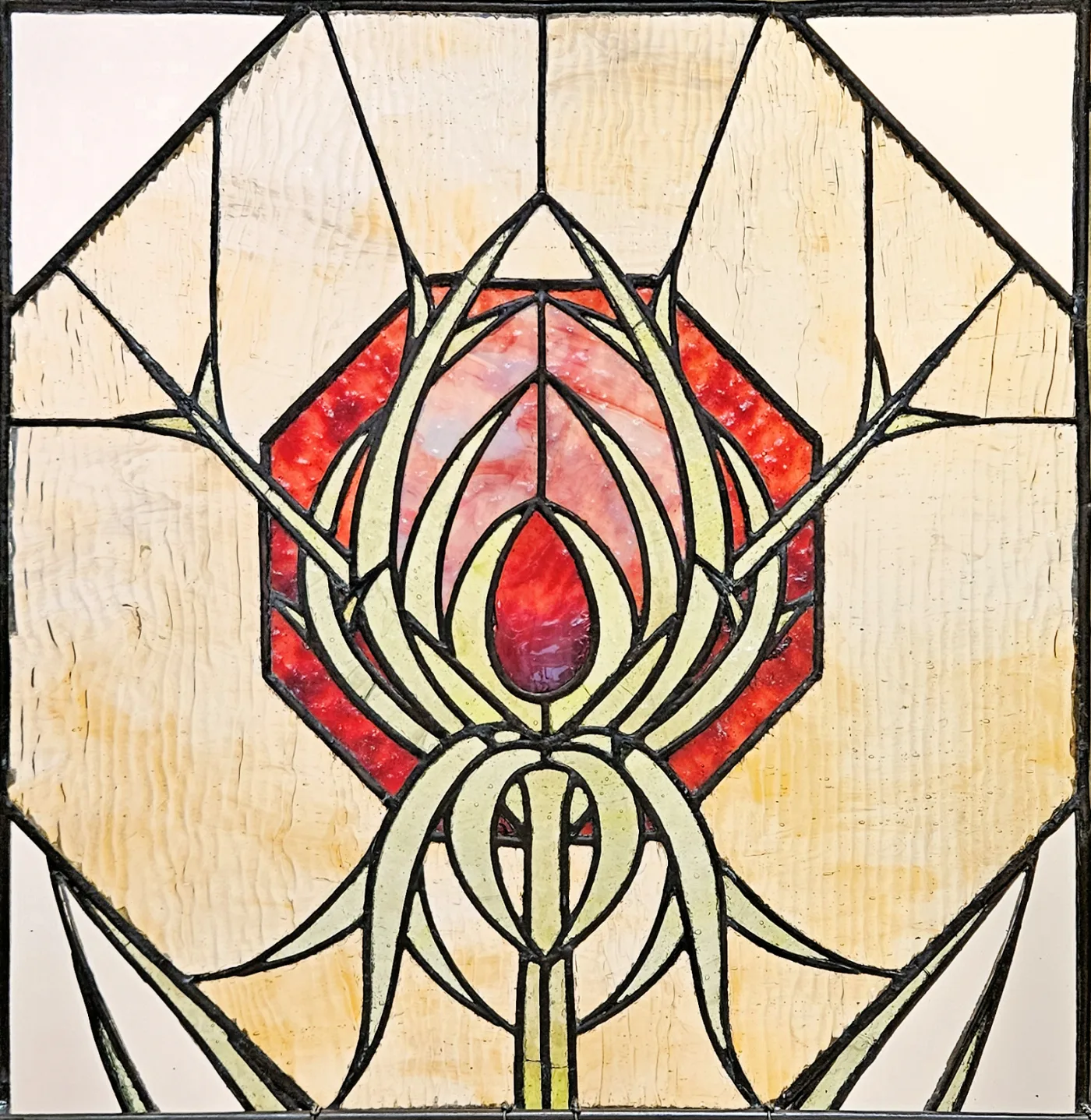 Top panel of a leaded window: a stylised red and cream blossom inside an octagon, framed by straight-edged geometric glass