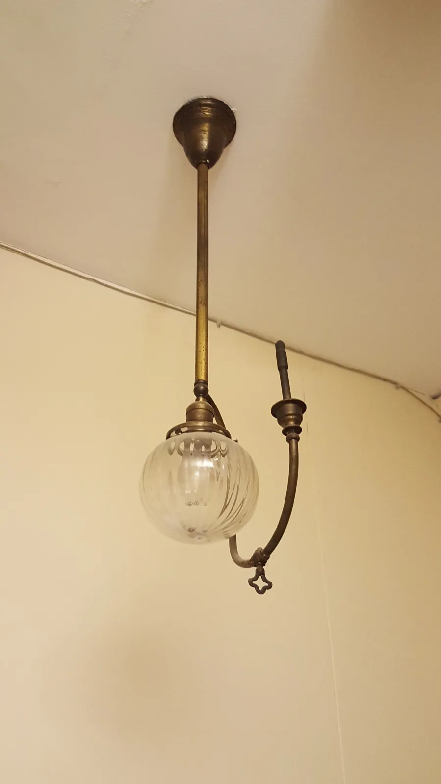Ceiling light fixture with one short arm carrying an upward globe and a second arm curving downward to a socket