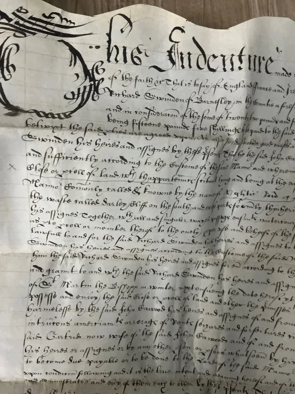 Sheet of aged parchment covered in dense secretary-hand script, headed with an elaborate calligraphic word, with a dark wax seal attached at the foot