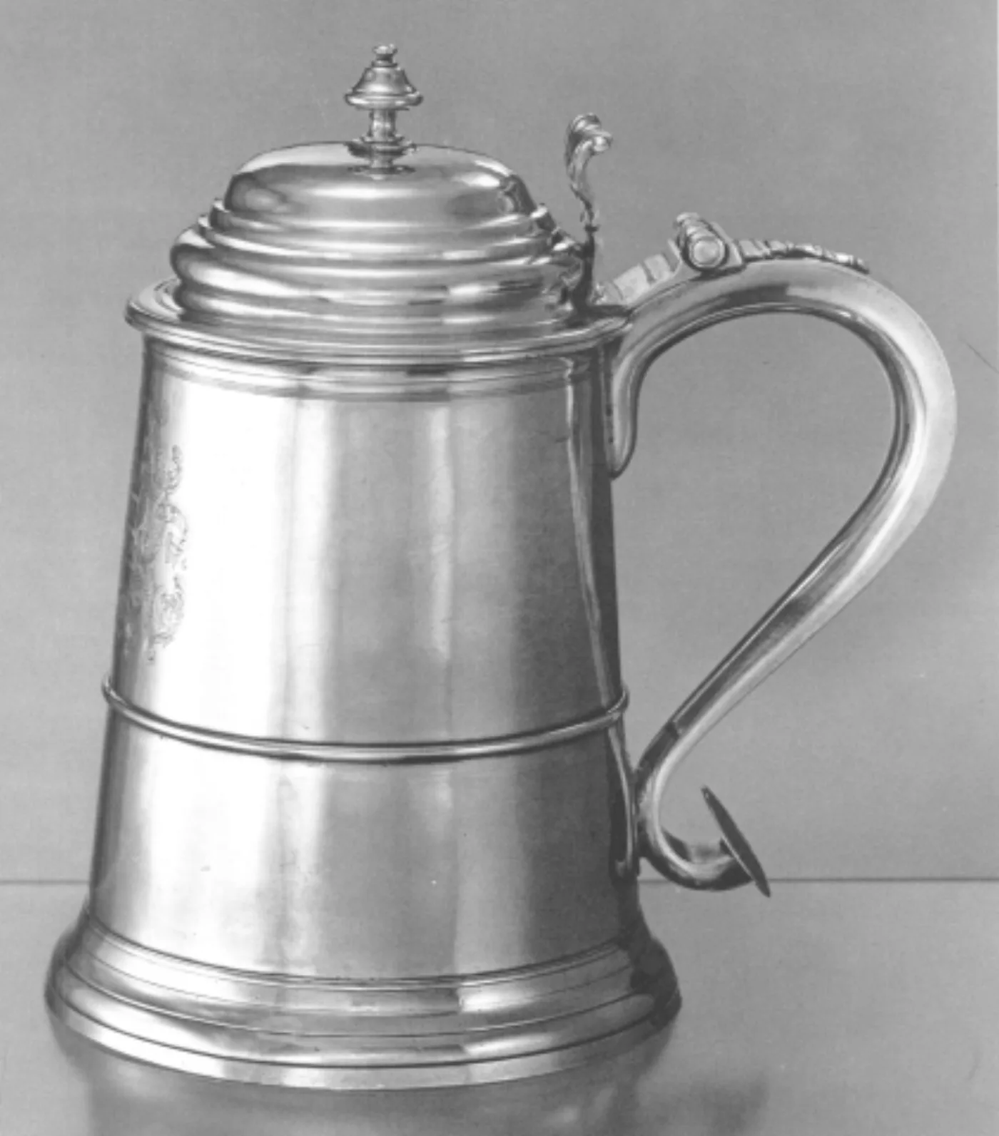 Plain pewter tankard with a domed hinged lid, scroll handle and stepped foot