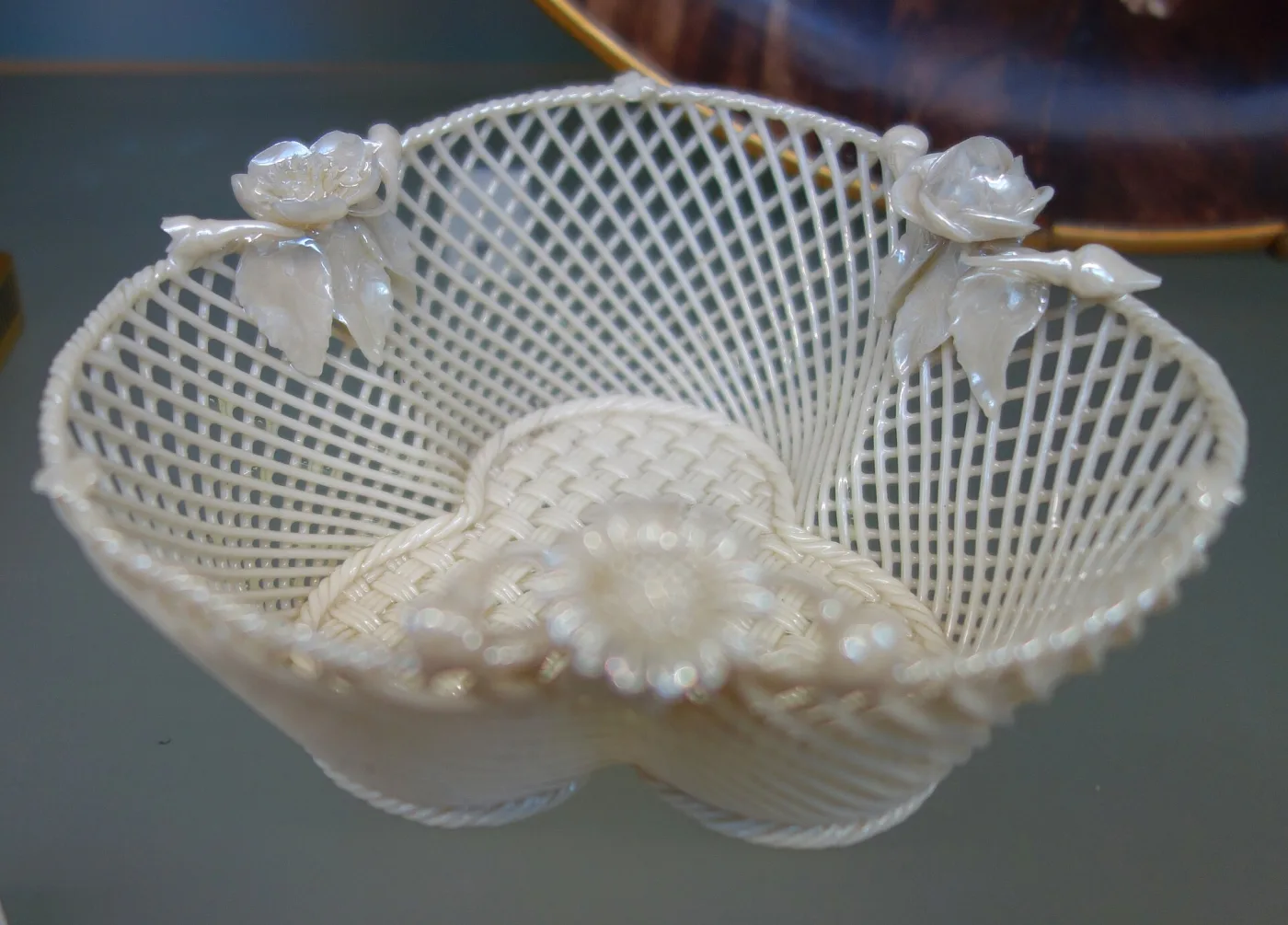 Shallow oval basket woven from fine white porcelain strands in an open lattice, its rim built up in three layers and applied with modelled roses and lily-of-the-valley