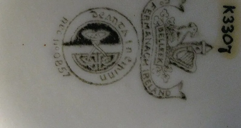 Printed mark in black on white porcelain showing a circular Gaelic-lettered roundel beside a device of a harp, an Irish wolfhound and a round tower above a banner reading Belleek Co Fermanagh Ireland