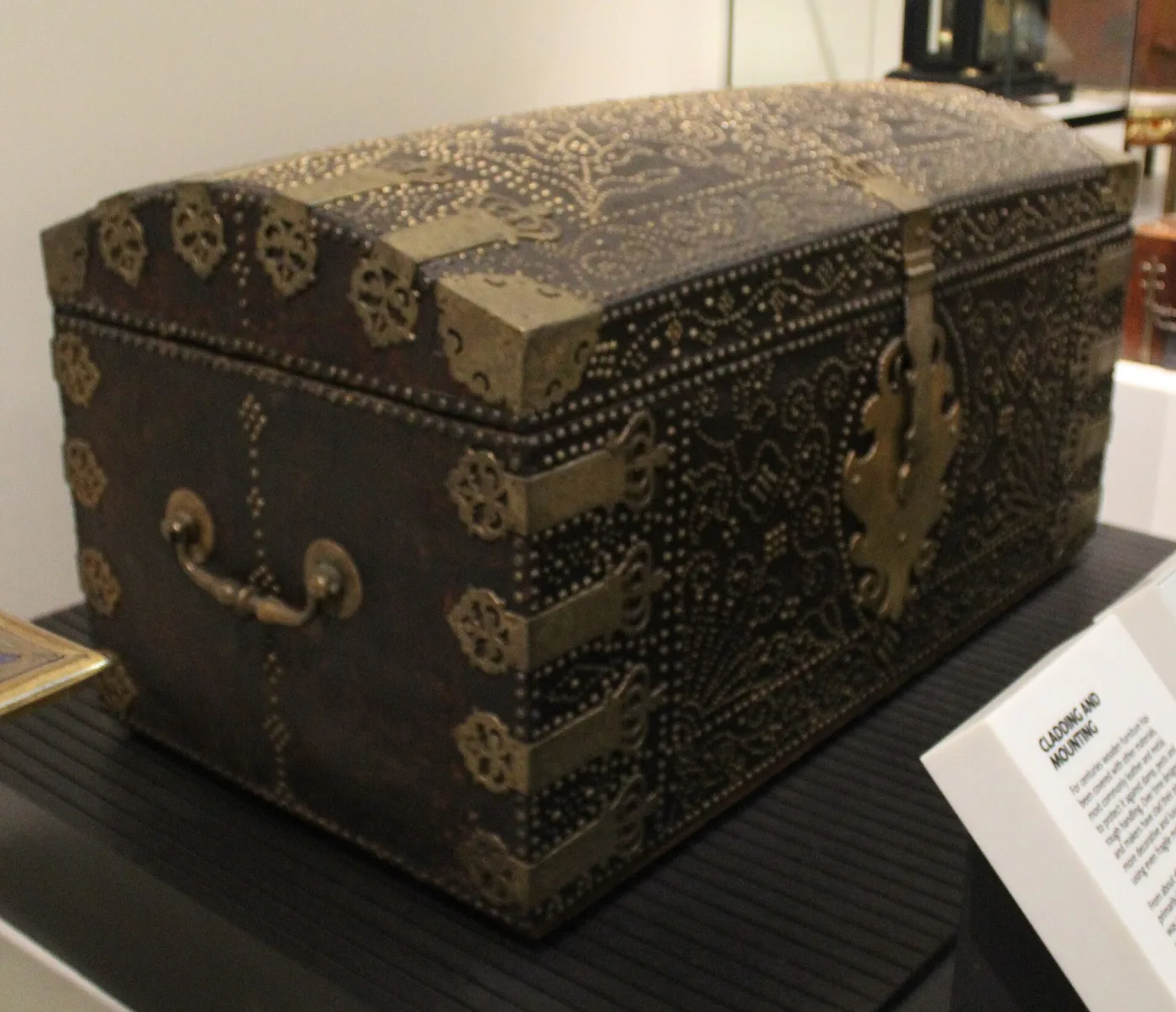 Domed travelling trunk covered in dark leather, ornamented all over with patterns of small brass nails, with brass corner mounts, a shaped lock plate and a swing handle at the end