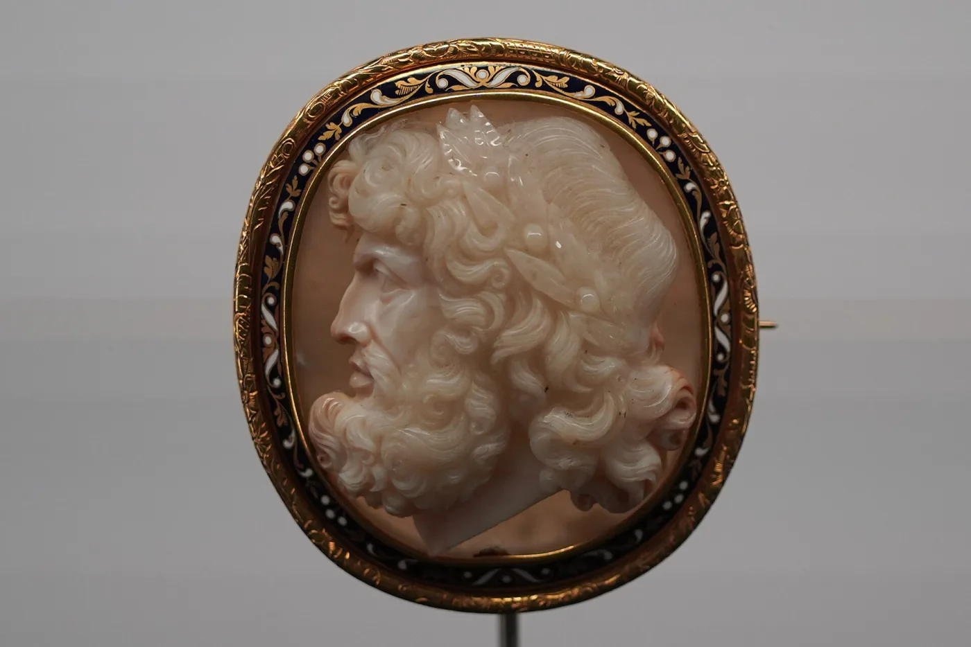 Oval brooch with a carved bearded profile of Jupiter in white against a warm brown ground, mounted in a gold frame banded with blue and white enamel