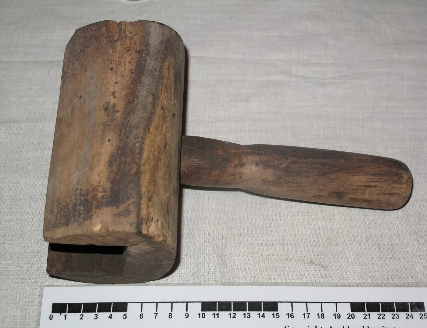 Mallet-shaped wooden butter mold with a rectangular hollow cut into the head, laid above a black-and-white centimetre scale
