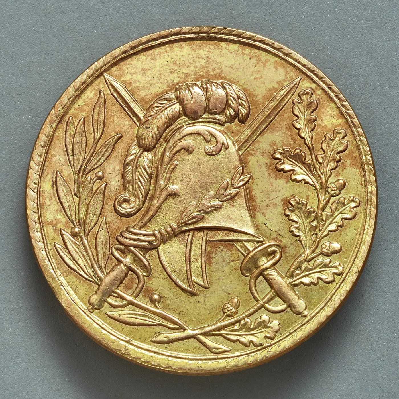 Gilt uniform button struck with a plumed classical helmet over a crossed sword and sabre, an olive branch to the left and an oak branch to the right, inside a roped rim