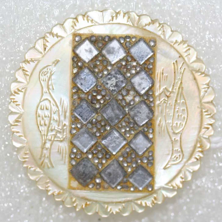 Mother-of-pearl button with a scalloped carved rim, an engraved bird on one side and a fish on the other, and a central rectangular panel of small faceted cut-steel studs laid in a diamond lattice