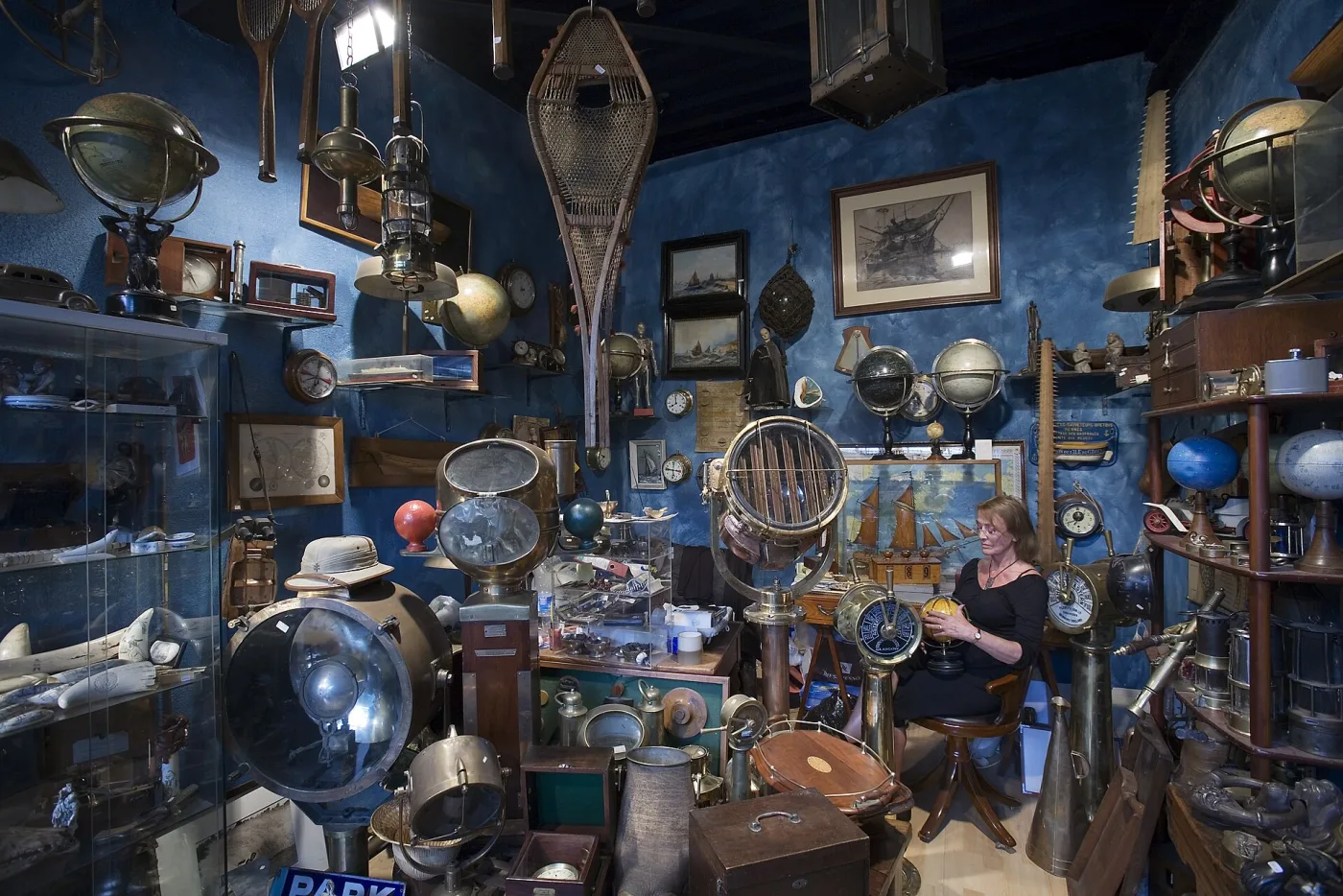 Crowded stall at a Paris flea market hung floor to ceiling with vintage suitcases, hat boxes, steamer trunks and leather bags, a dealer seated at the back