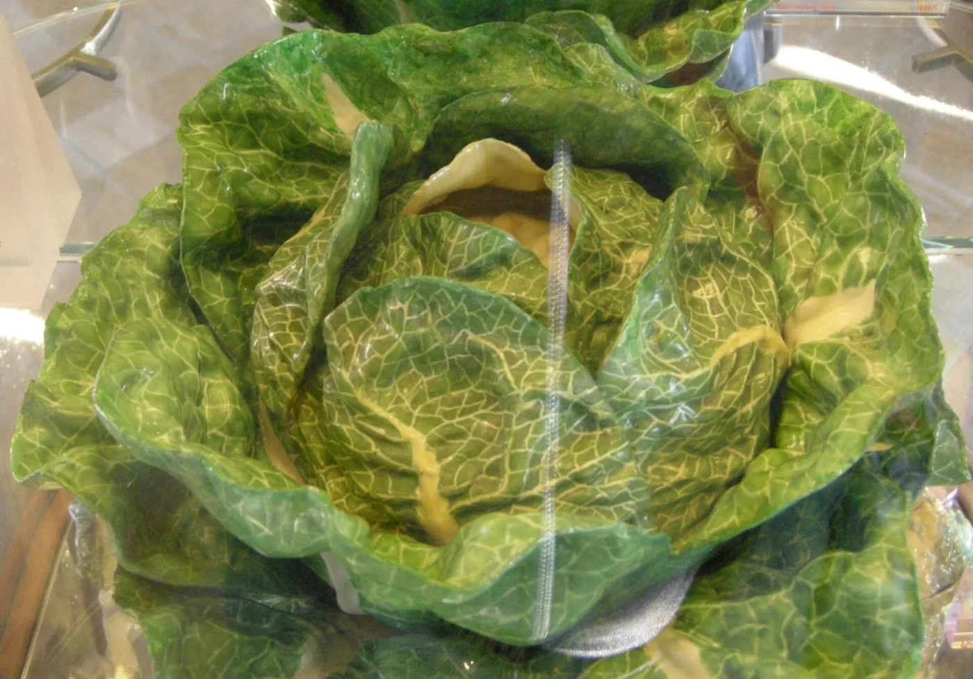 Faience tureen shaped as a cabbage with loose curling green outer leaves and a yellow heart, seen through display glass