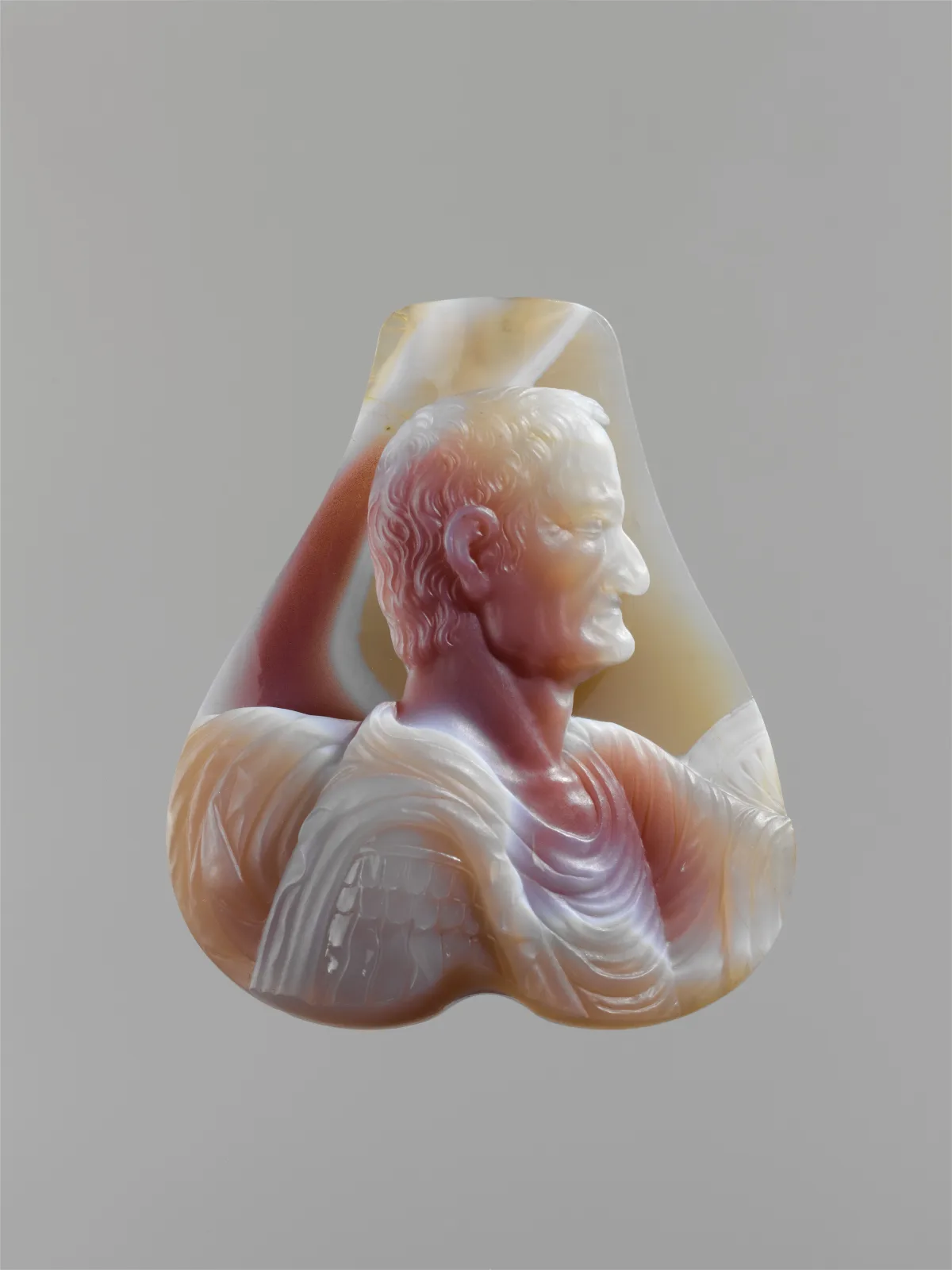 Unmounted agate cameo carved in high relief as the bust of a Roman emperor in armour and drapery, the stone running from milky white through peach and deep rust-red, the blank left in an irregular free-form outline