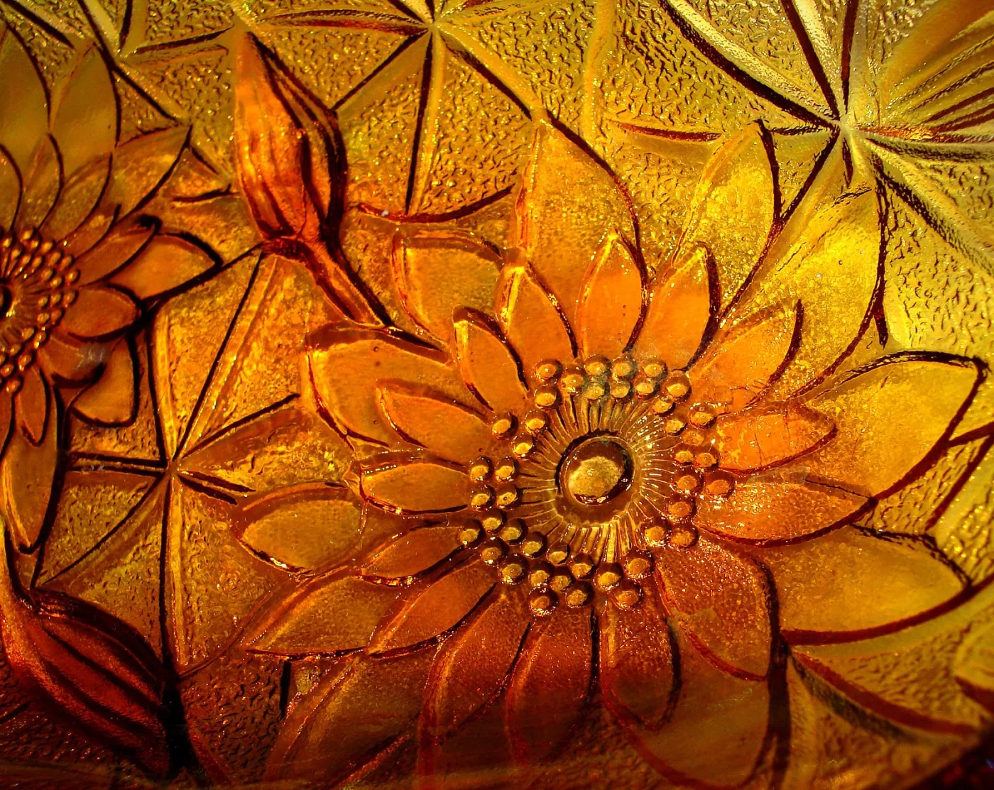 Extreme close-up of moulded glass sunflowers and leaves, the surface breaking into orange, gold and amber where the light catches the raised petals