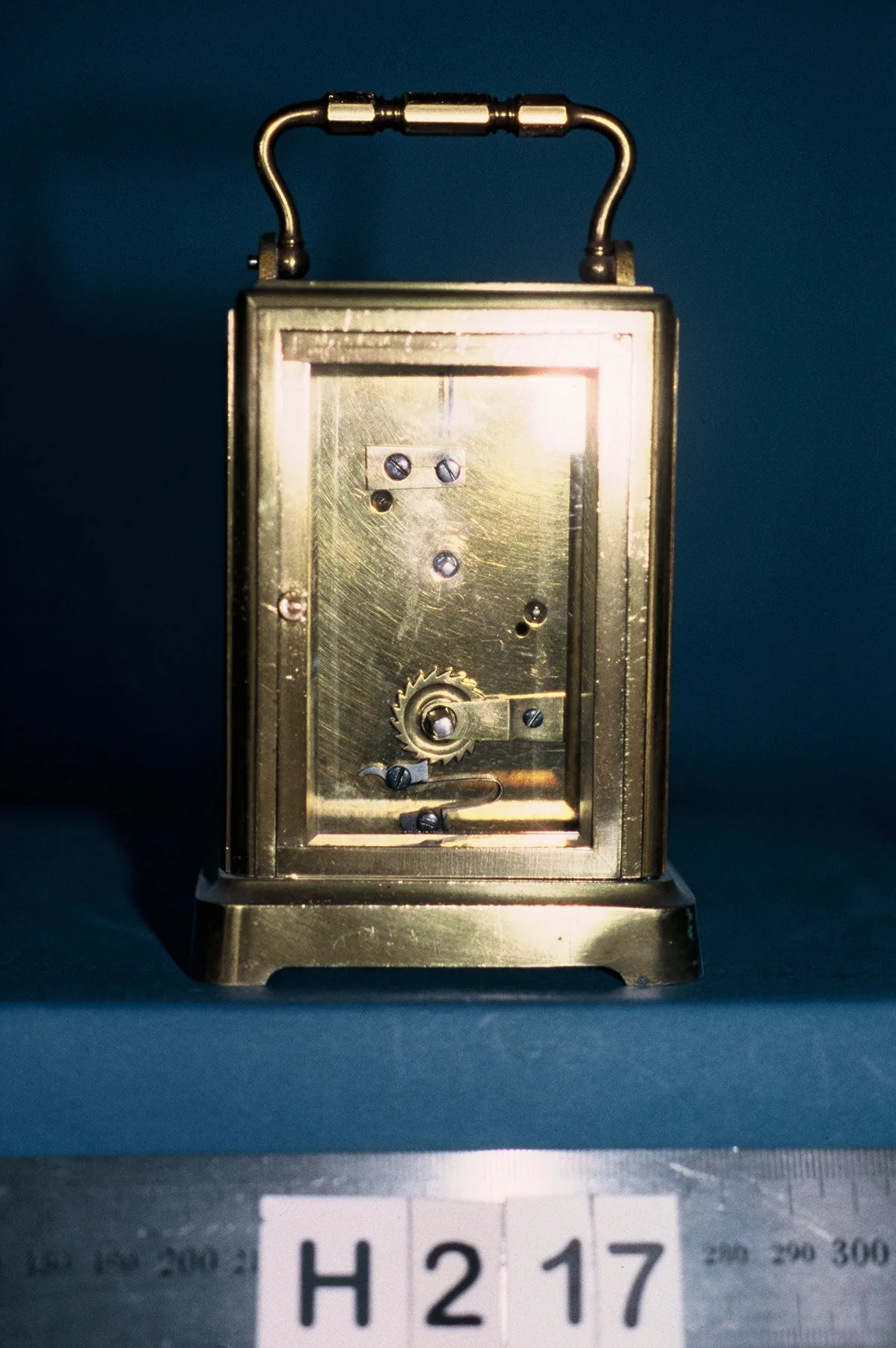 Rear view of the same brass carriage clock showing a plain gilt backplate, screwed fixings, a ratchet wheel and a setting lever