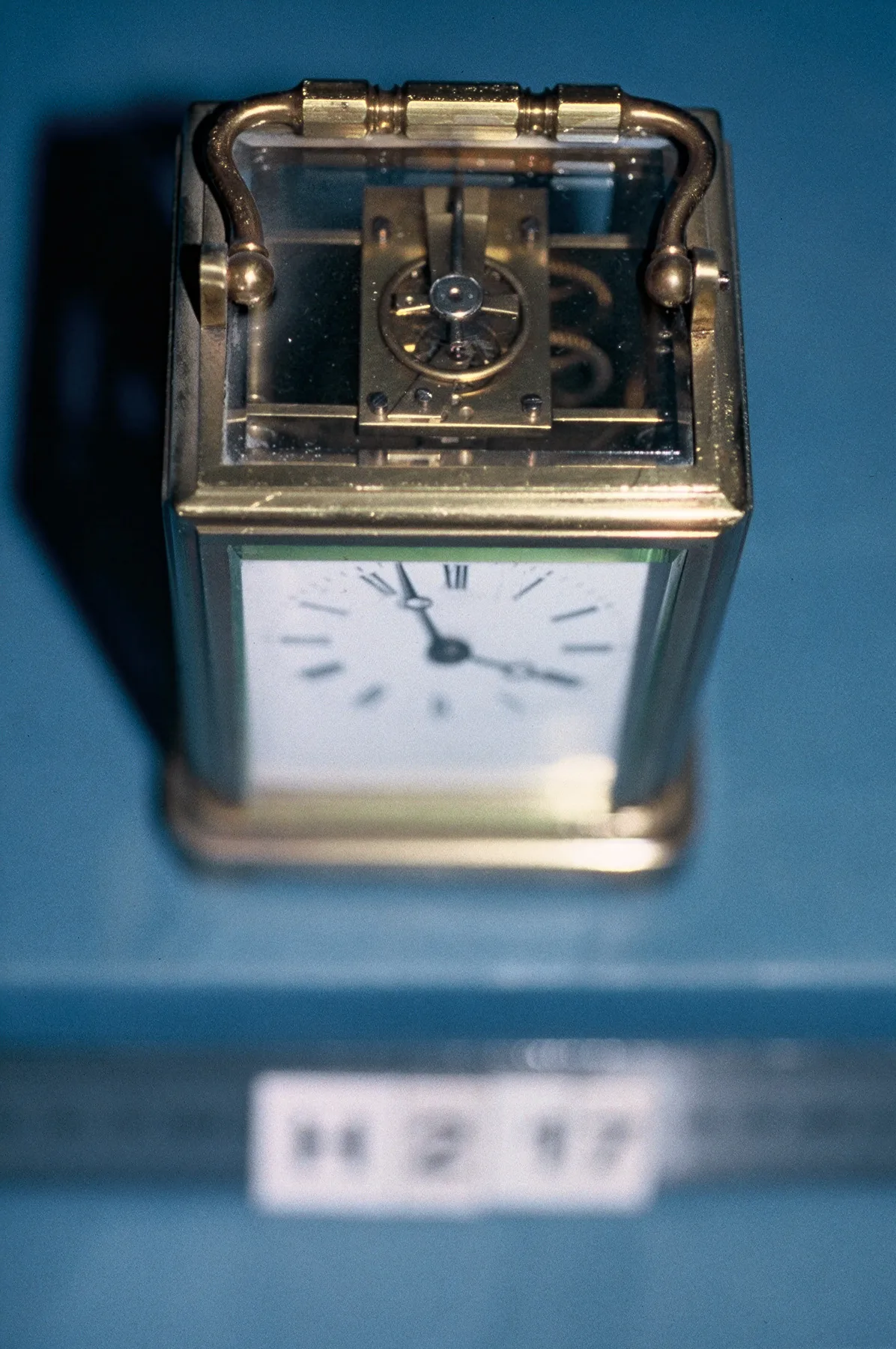 Looking down through the glazed top of a brass carriage clock at the platform escapement, with the balance wheel and its spring visible under the glass