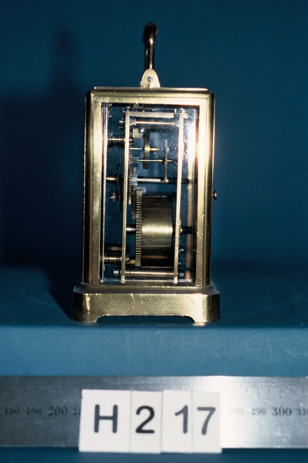 Side view through the glass of a brass carriage clock, showing the going train wheels and a single large mainspring barrel between the plates