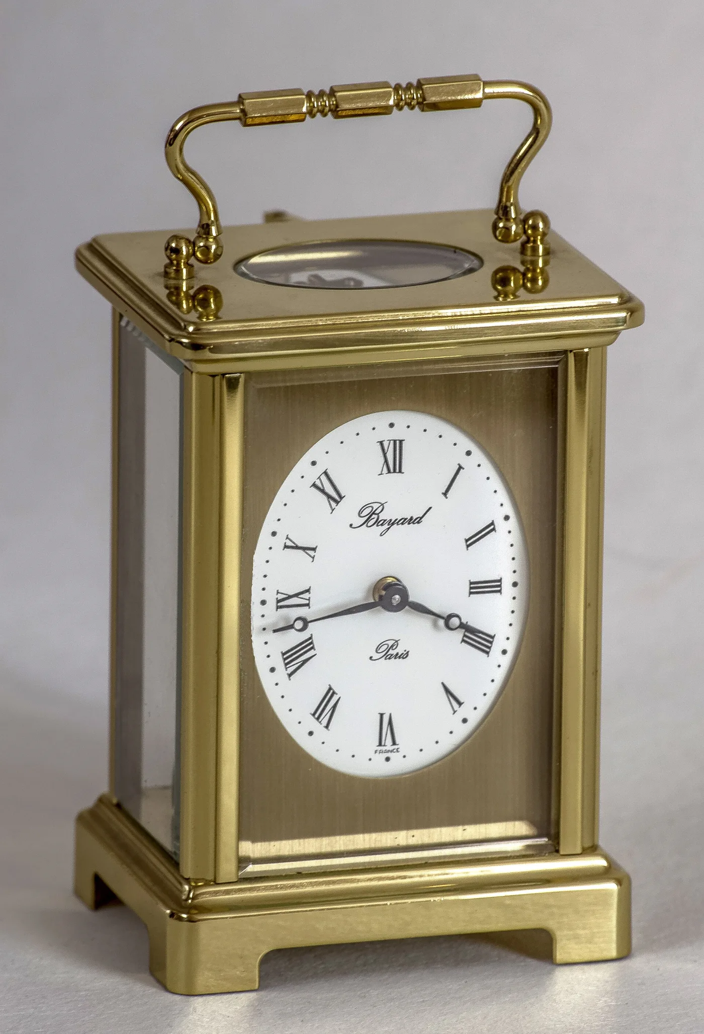 Small brass carriage clock with an oval white enamel dial signed Bayard Paris on a brushed gilt mask, and a glazed oval window in the top plate