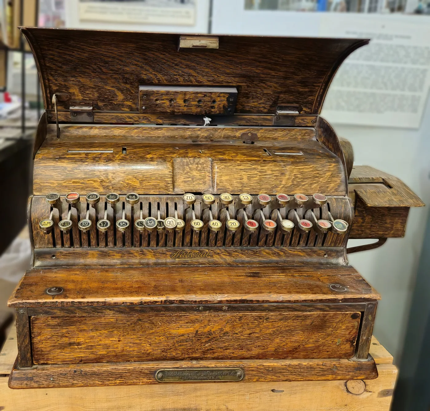 Oak-cased National cash register with its hinged lid raised, exposing rows of levers, springs and racks above the keyboard