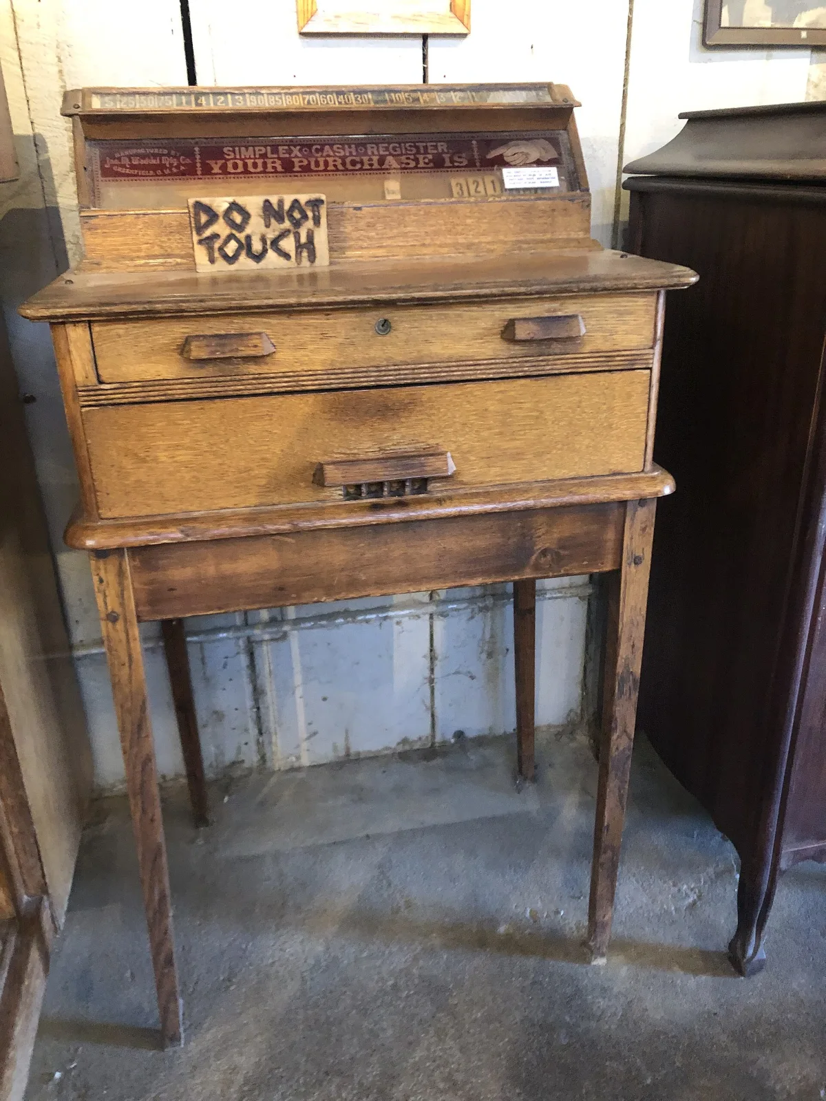 Tall oak-cased cash register on turned legs with a small sign reading do not touch, in a western history museum