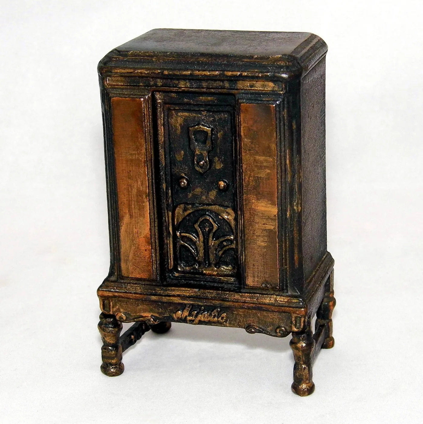 Cast iron money bank modelled as a 1930s radio console on turned legs, painted dark with a gilt speaker grille and three tuning knobs, with a coin slot in the top