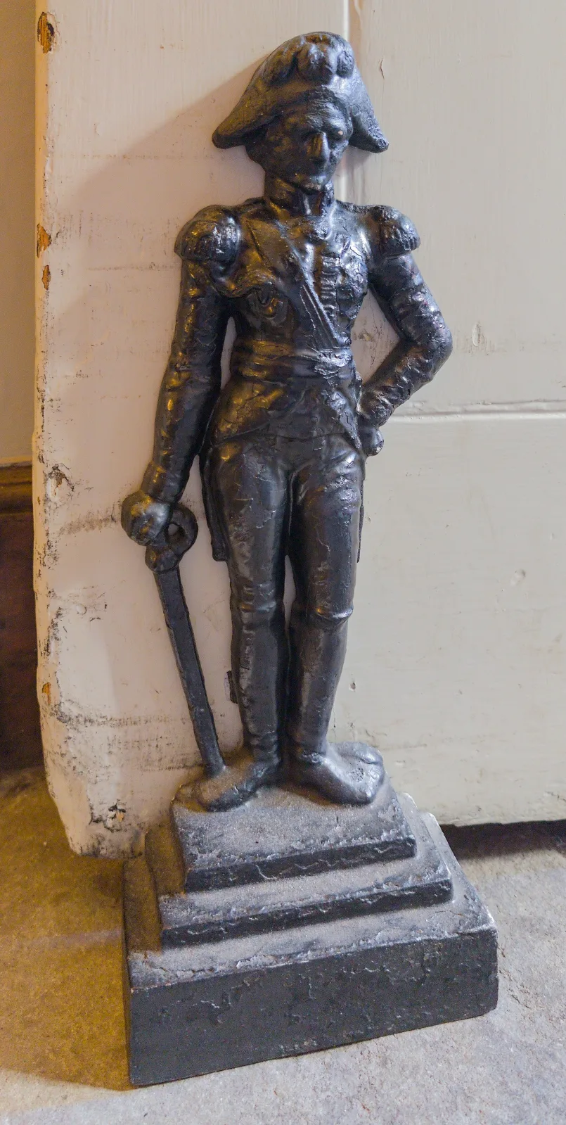 Cast iron figural doorstop of a standing naval officer in a bicorne hat and full-dress coat with one arm behind his back, on a stepped rectangular base, set against a wall