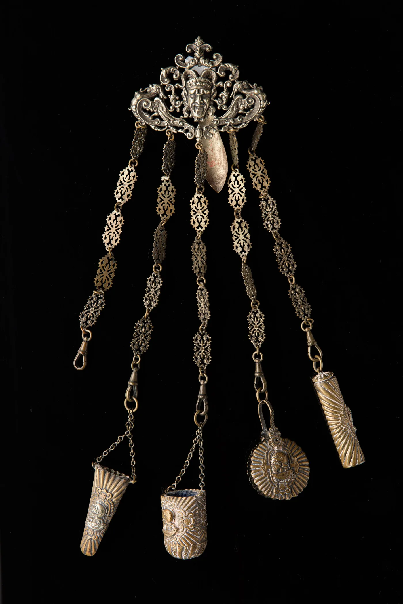Gilded silver chatelaine with a satyr-mask belt clip and five chains carrying decorated thimble holders and a needle case