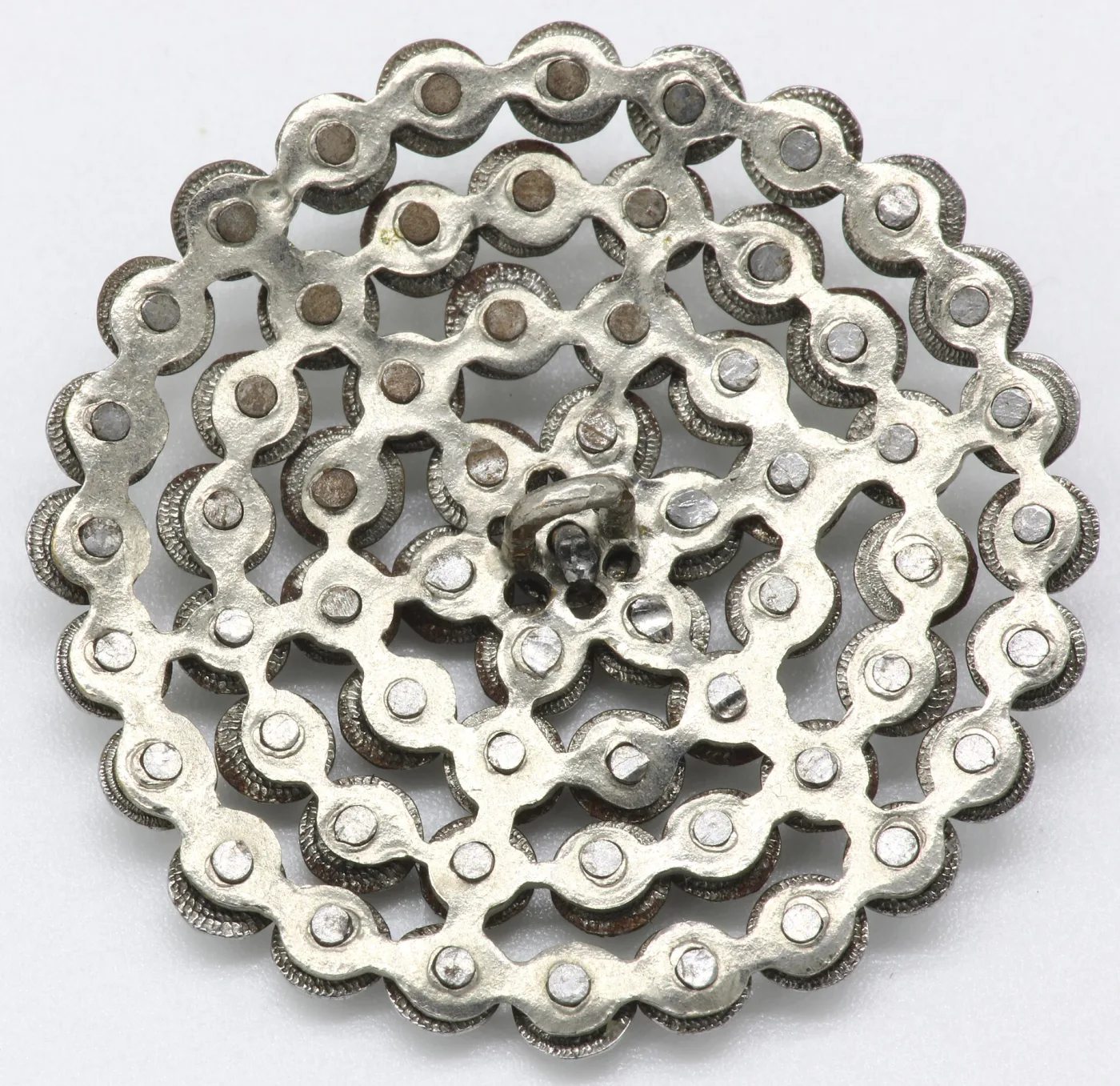Reverse of a cut steel button showing a pierced openwork plate with a separate rivet head behind every stud