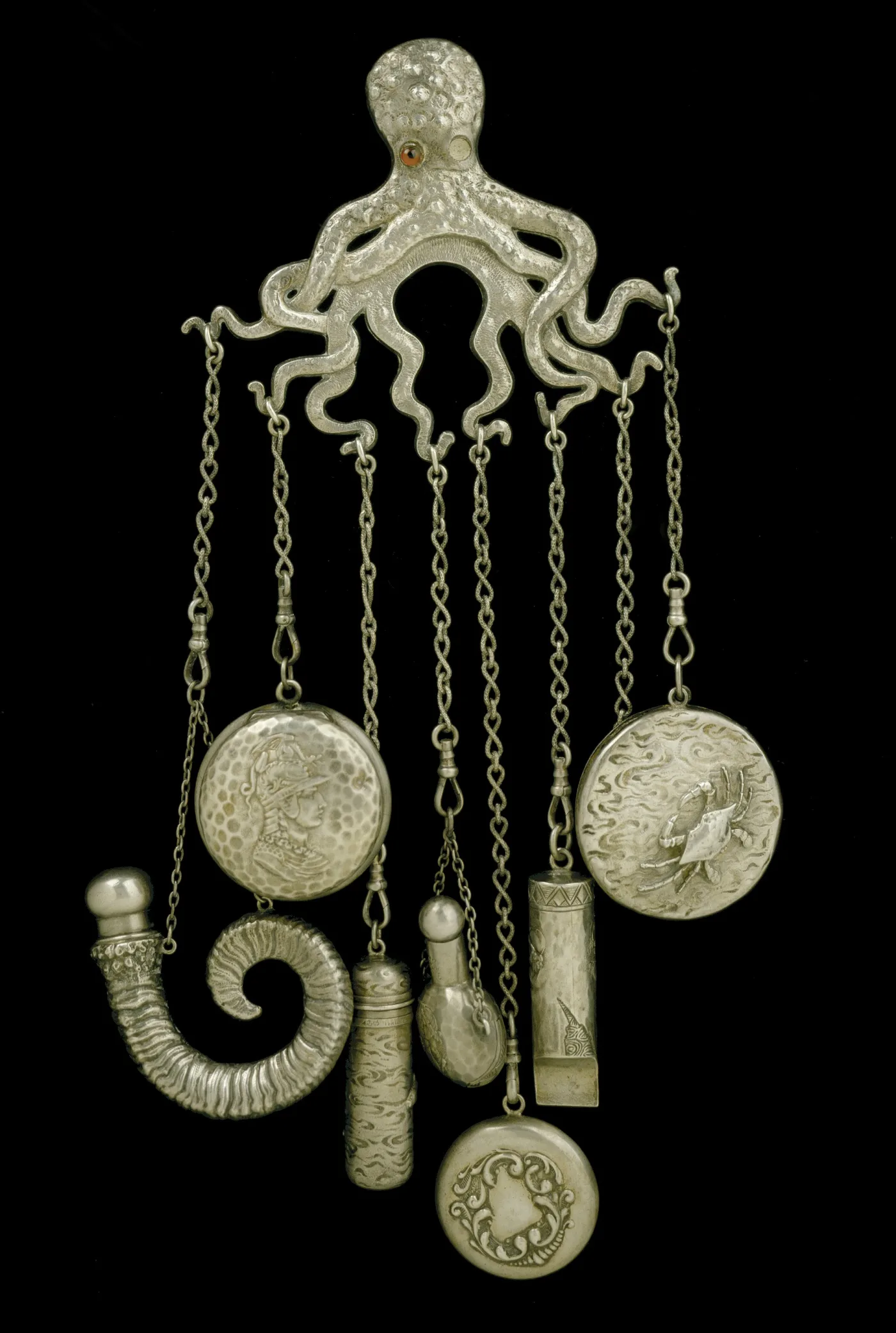 The same octopus chatelaine design with its attachments in place, including a scent bottle, a mirror, a whistle, a cylindrical case and two decorated discs