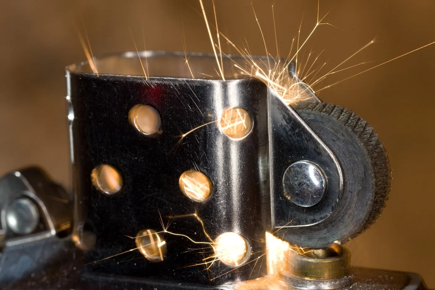 Close-up of a lighter insert at the moment of striking, showing a perforated chimney, a knurled flint wheel on a riveted pivot and a shower of sparks