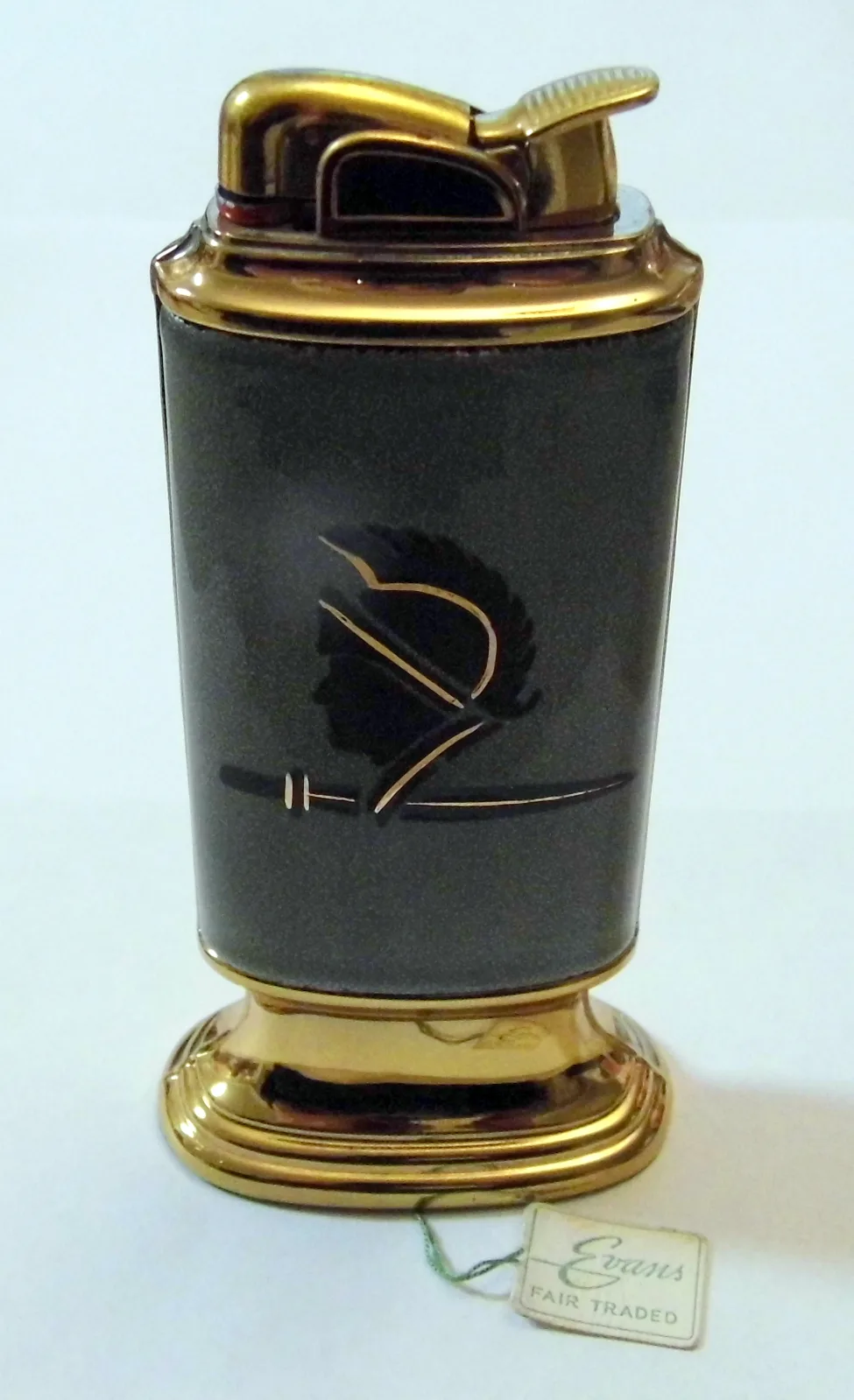 Column-shaped table lighter with a gilt lift-arm top and stepped gilt foot, the grey body panel decorated with a black and gilt classical helmet and sword, with a small paper tag tied to the base reading Evans Fair Traded