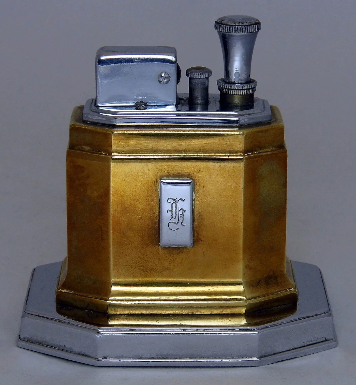 Octagonal table lighter with a gilt body on a stepped chrome base, a hinged chrome cover over the ignition unit, and a tall knurled chrome wand standing upright at the right