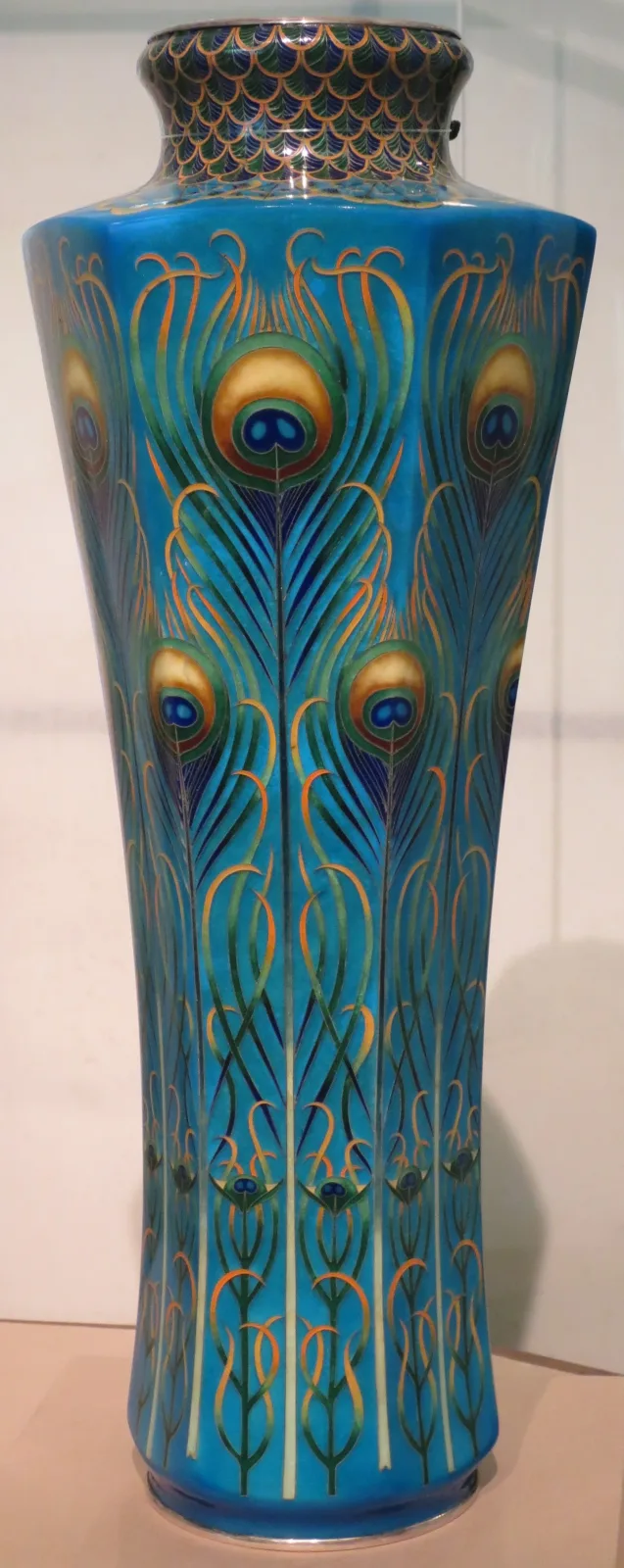 A tall slender cloisonne vase covered in an overlapping peacock-feather pattern in blues and greens