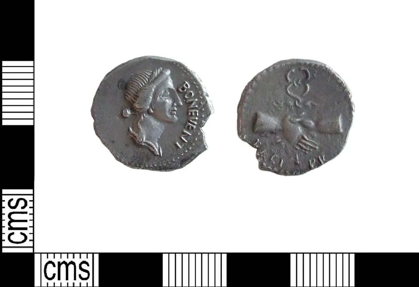 Two views of a small worn silver coin against a centimetre scale: on the left a head in profile with a legible legend, on the right a much more worn design of standing figures