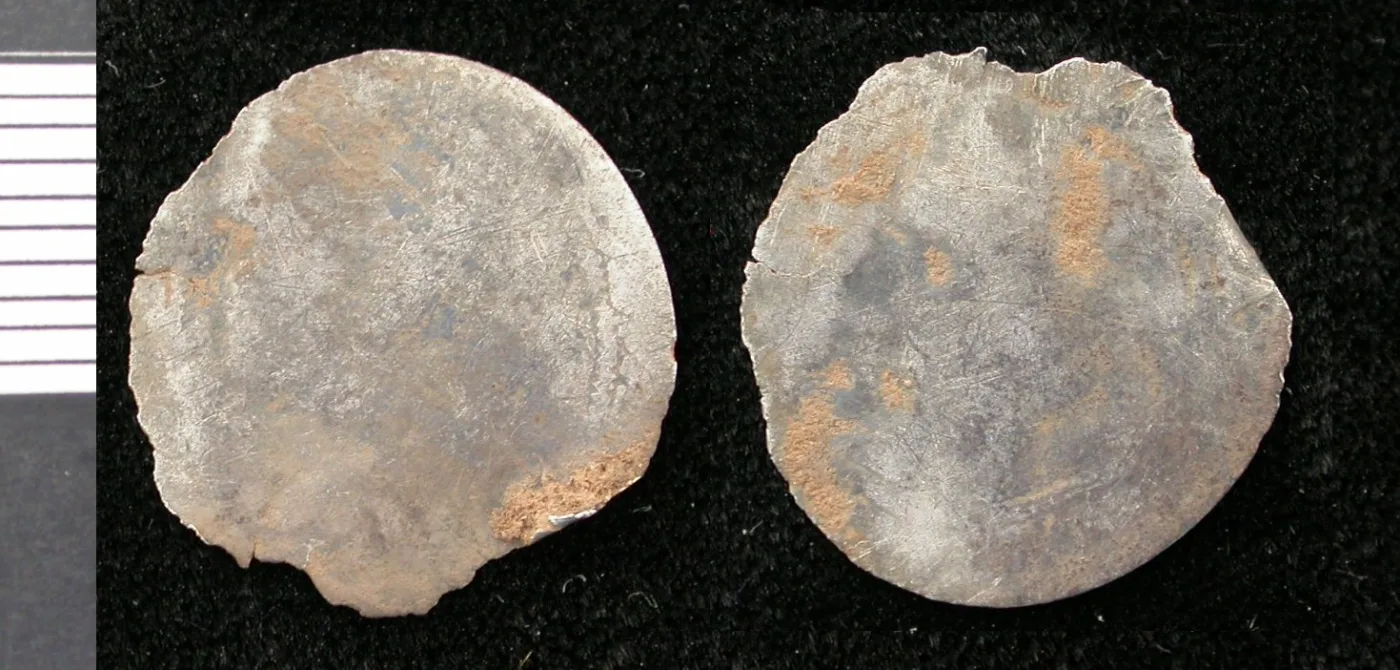 Two faces of a small, thin, irregular silver disc with a ragged edge, both sides completely smooth and blank with no trace of any design