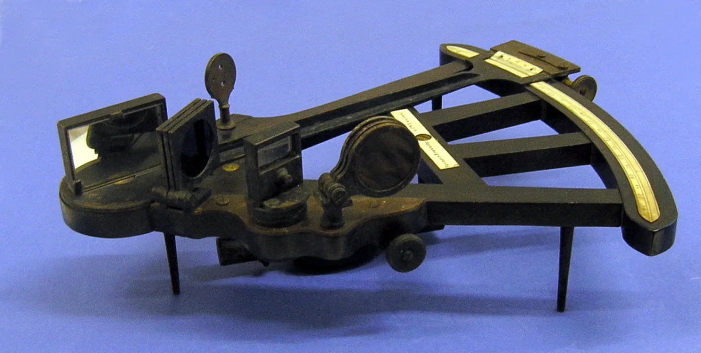 The same kind of octant seen from the side and slightly above, showing the depth of its wooden frame, the two mirrors standing proud of it, the index arm bridging them and three small feet holding it clear of the surface