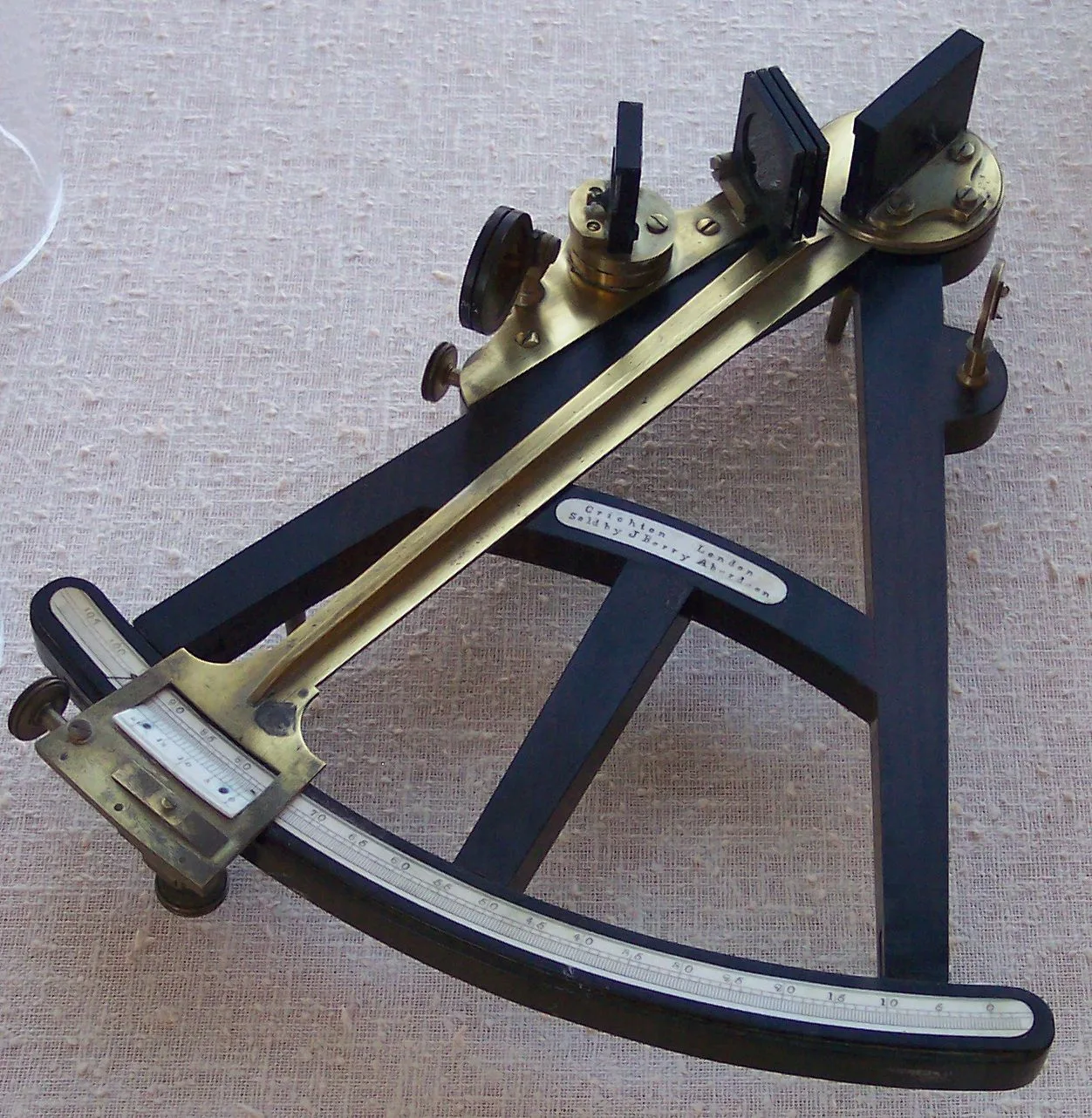 Octant with a black wooden triangular frame, a graduated arc along its lower edge, a pivoted brass index arm with a vernier scale, two mirrors and a set of coloured shade glasses, with a small inscribed plate on the crossbar