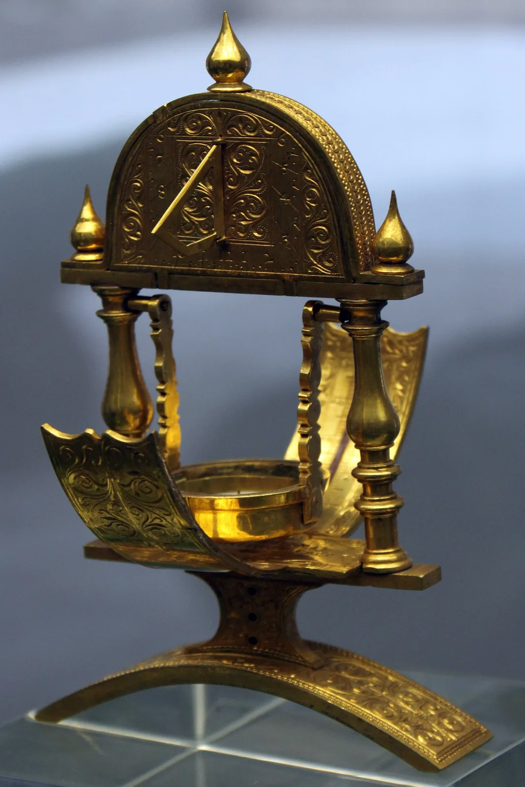 Gilt-brass instrument of 1602 with an engraved circular plate carrying a compass and sundial, a hinged sighting arm and a decorated stand with turned supports
