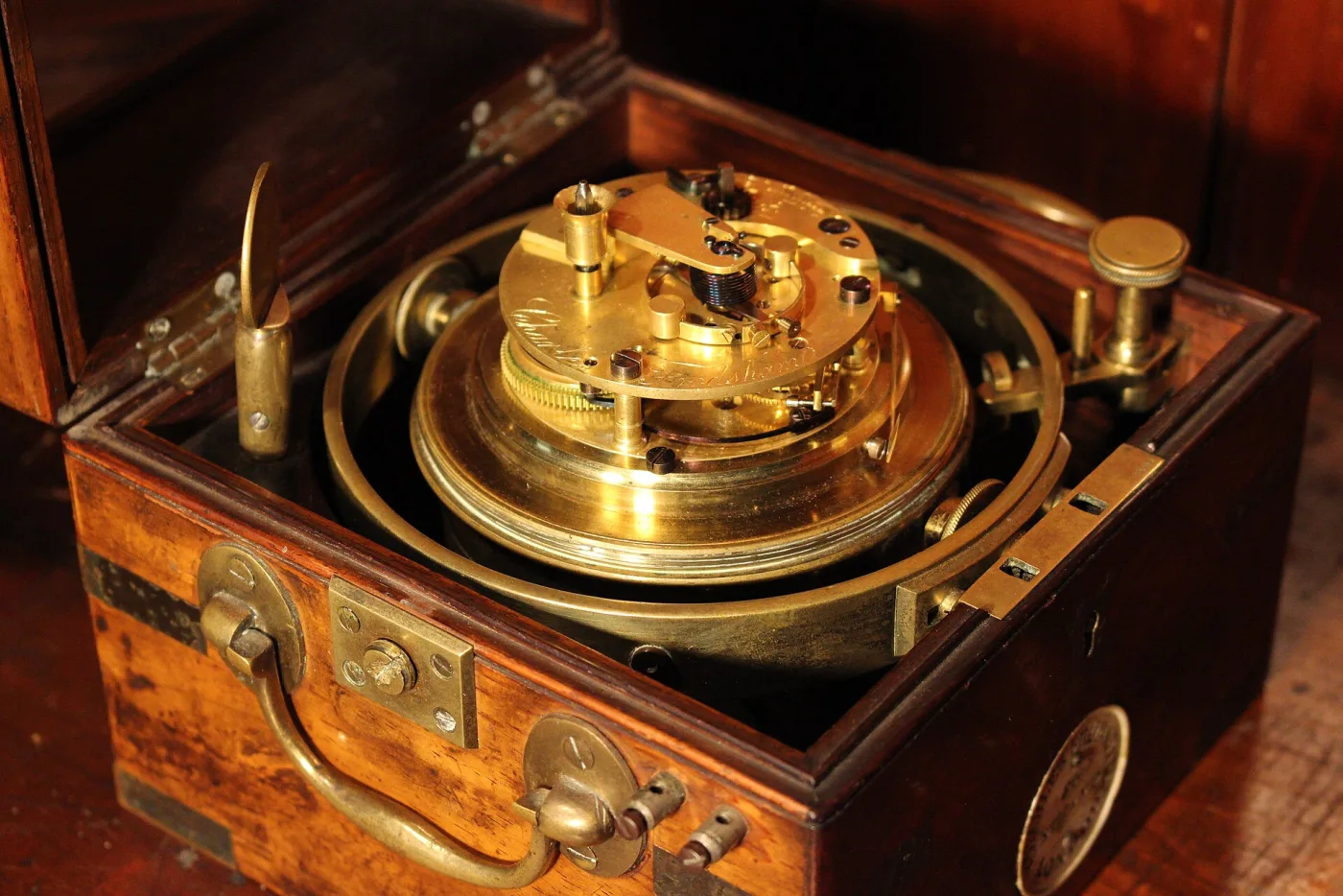 Gilt chronometer movement seen from above, mounted in a gimbal ring inside a mahogany box with the lid open, showing the fusee, the balance and the levers of the escapement