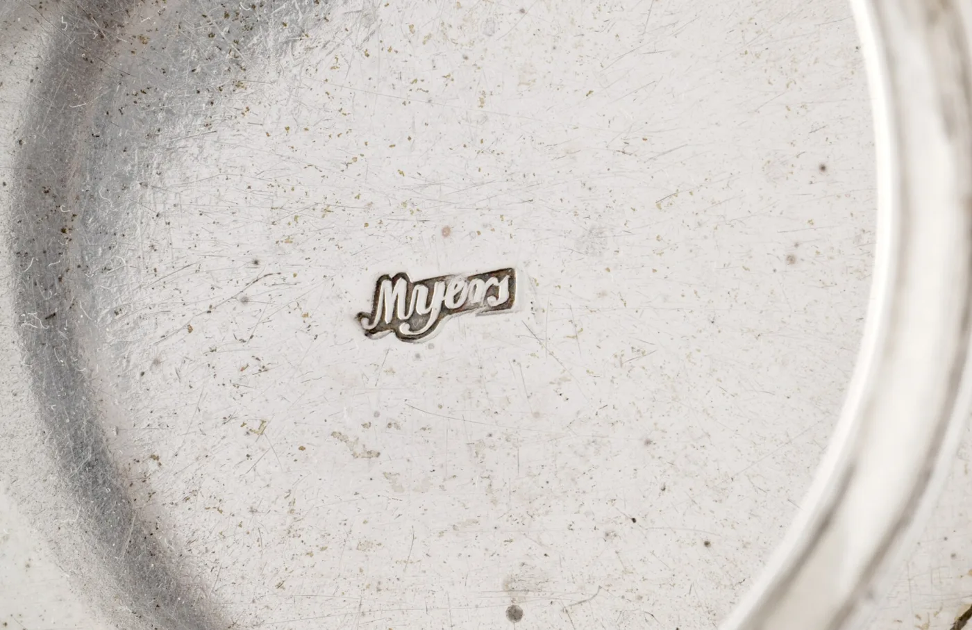 Close-up of a silver surface struck with a crisp script maker's mark reading Myers inside a shaped cartouche, surrounded by fine polishing scratches