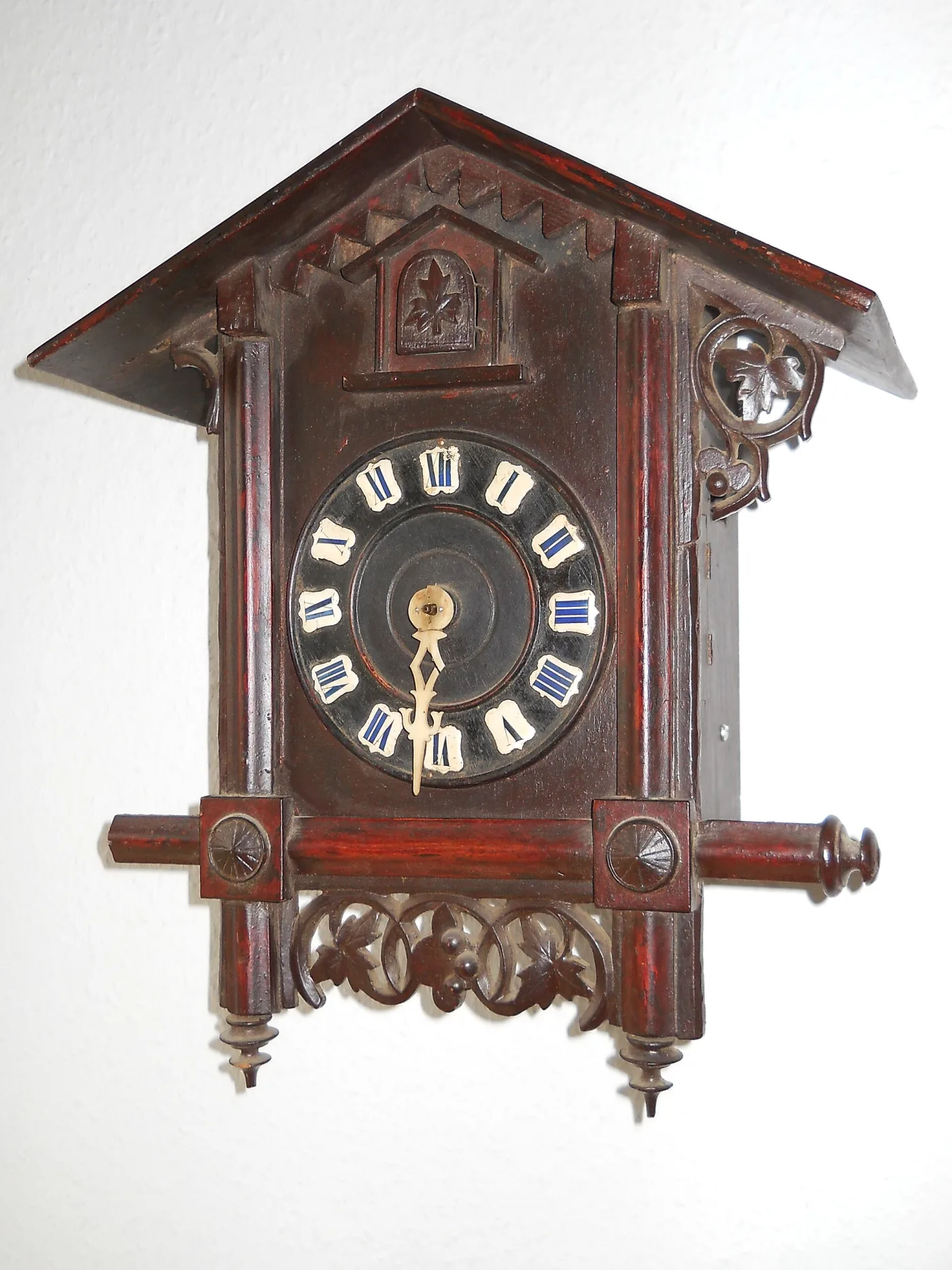 Dark stained Bahnhausle cuckoo clock with a pitched gable roof, sawtooth bargeboard, turned corner posts and a small carved cuckoo door above the dial