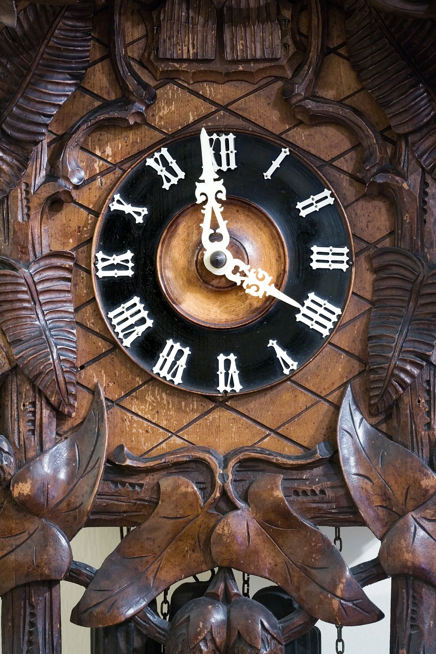Close-up of a carved cuckoo clock dial: a black painted wooden ring with applied cream bone Roman numerals and pierced bone hands