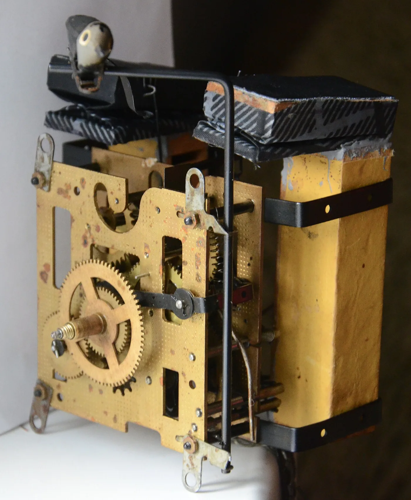 Cuckoo clock movement removed from its case, showing brass plates and gearing with two cloth-gusseted bellows lying on top and the bird on its wire lever
