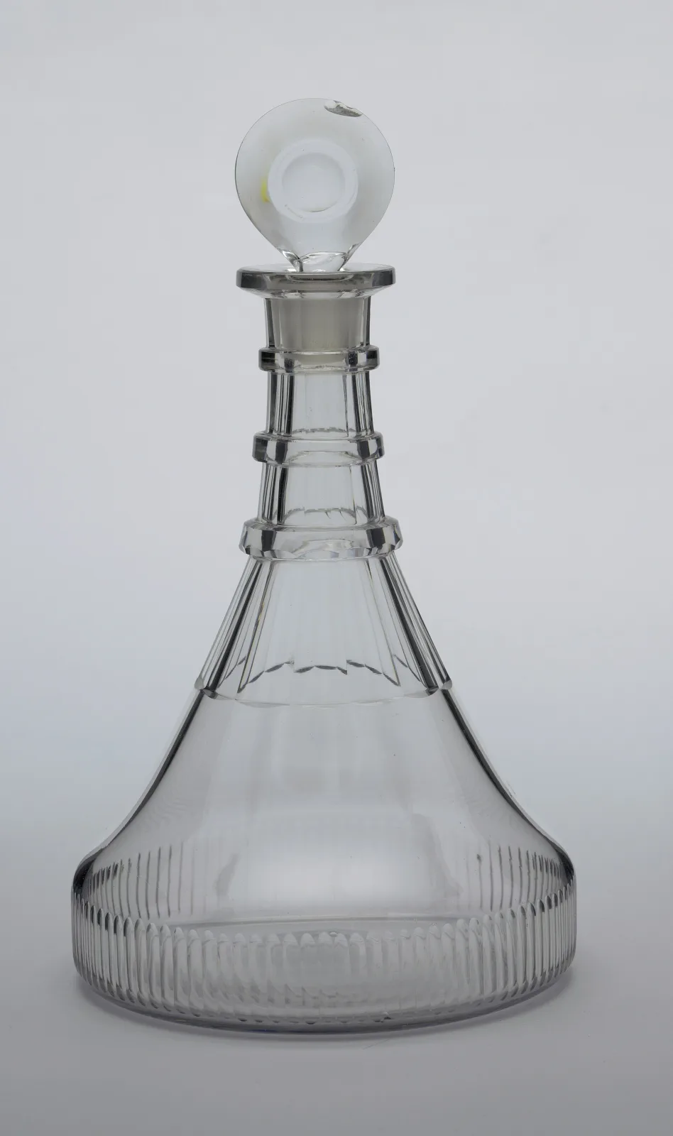 Decanter with a very broad flat base narrowing steeply to a tall neck, the base cut with close vertical comb flutes and the neck with long tapered flutes interrupted by three flat rings, under a flat cut disc stopper
