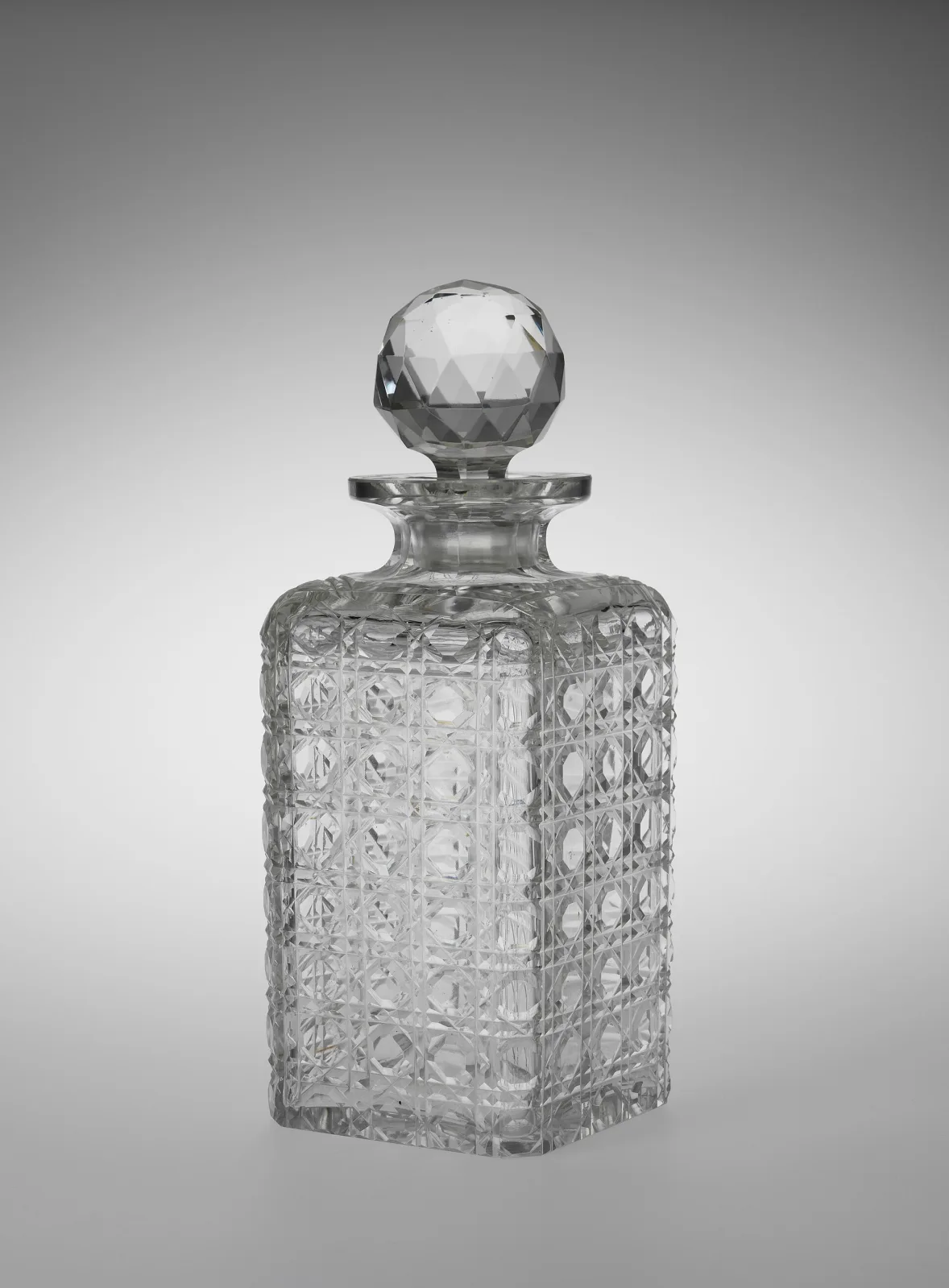 Square-sectioned decanter cut all over with rows of raised rounded bosses, with a short ringed neck and a faceted ball stopper