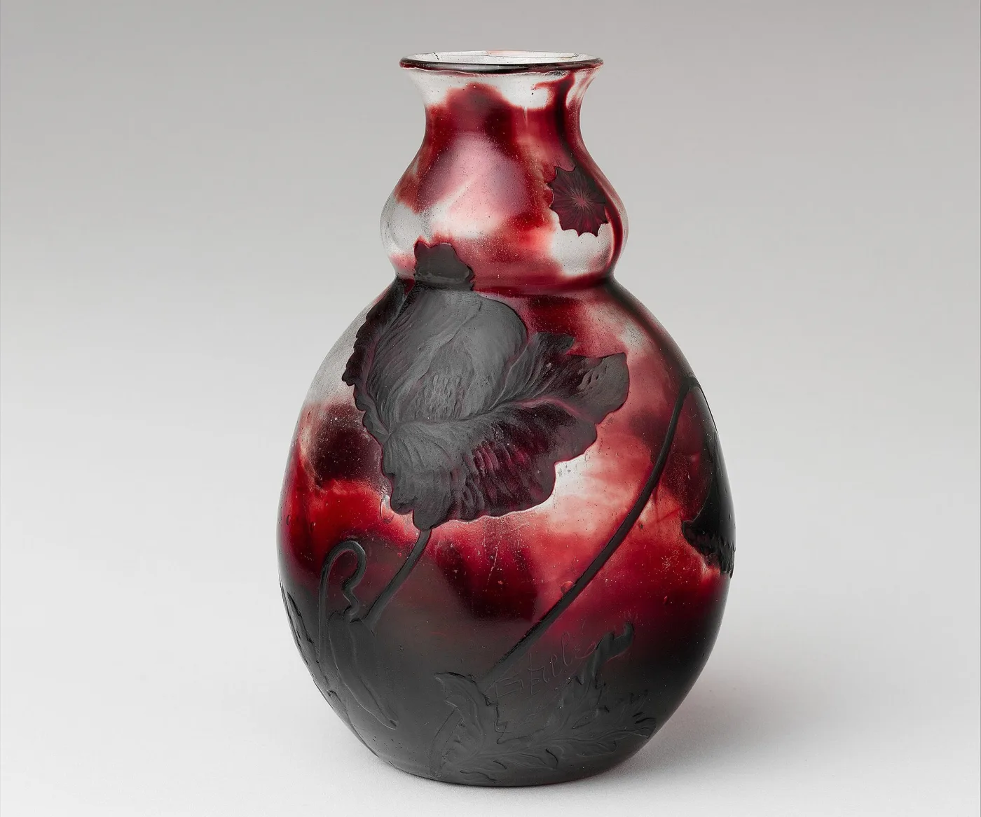 Double-gourd glass vase in mottled deep red and white, a dark poppy and its leaves carved in relief across the body, with the maker's cursive signature cut into the decoration among the lower leaves