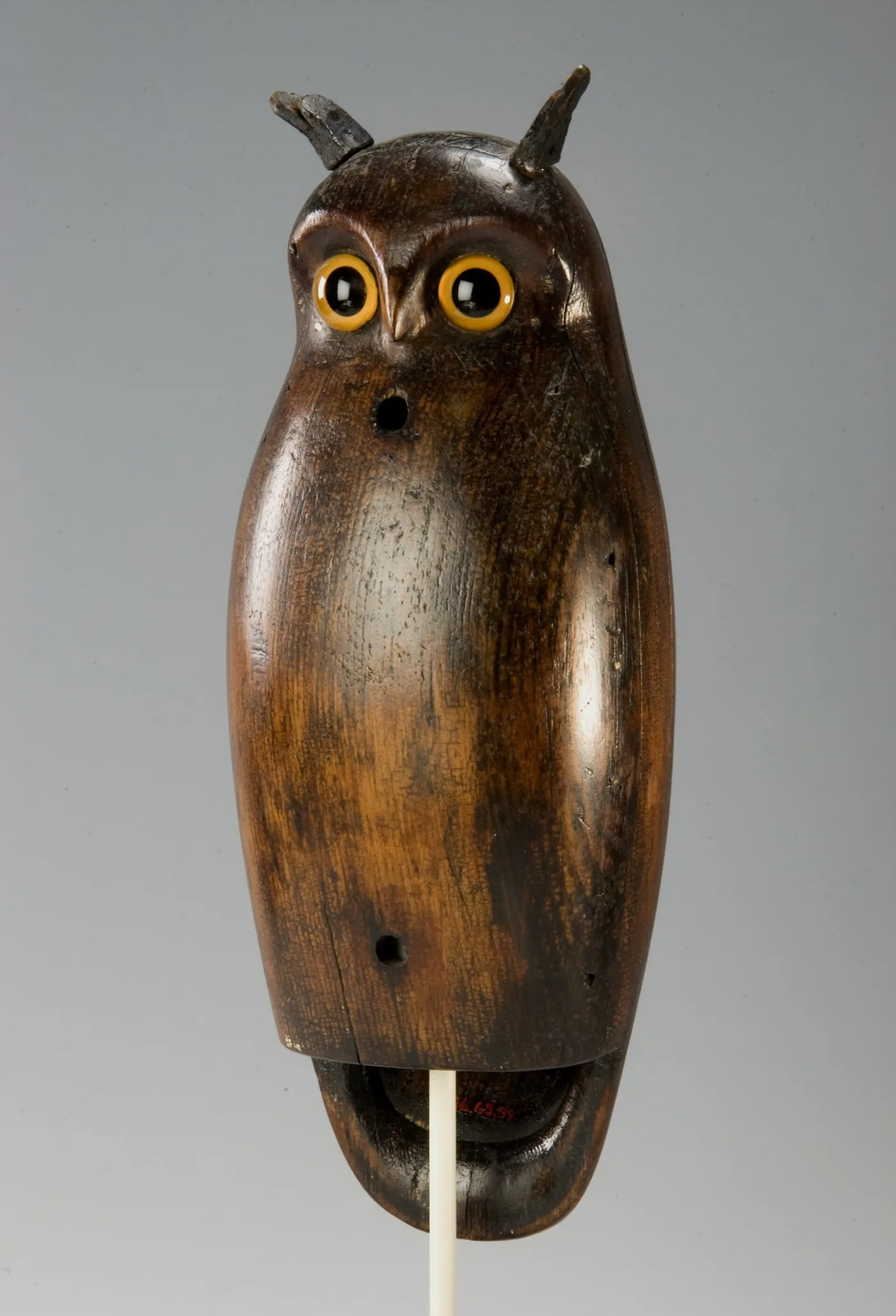 Carved wooden owl decoy with tufted ears, yellow glass eyes and a dark polished body, mounted on a rod