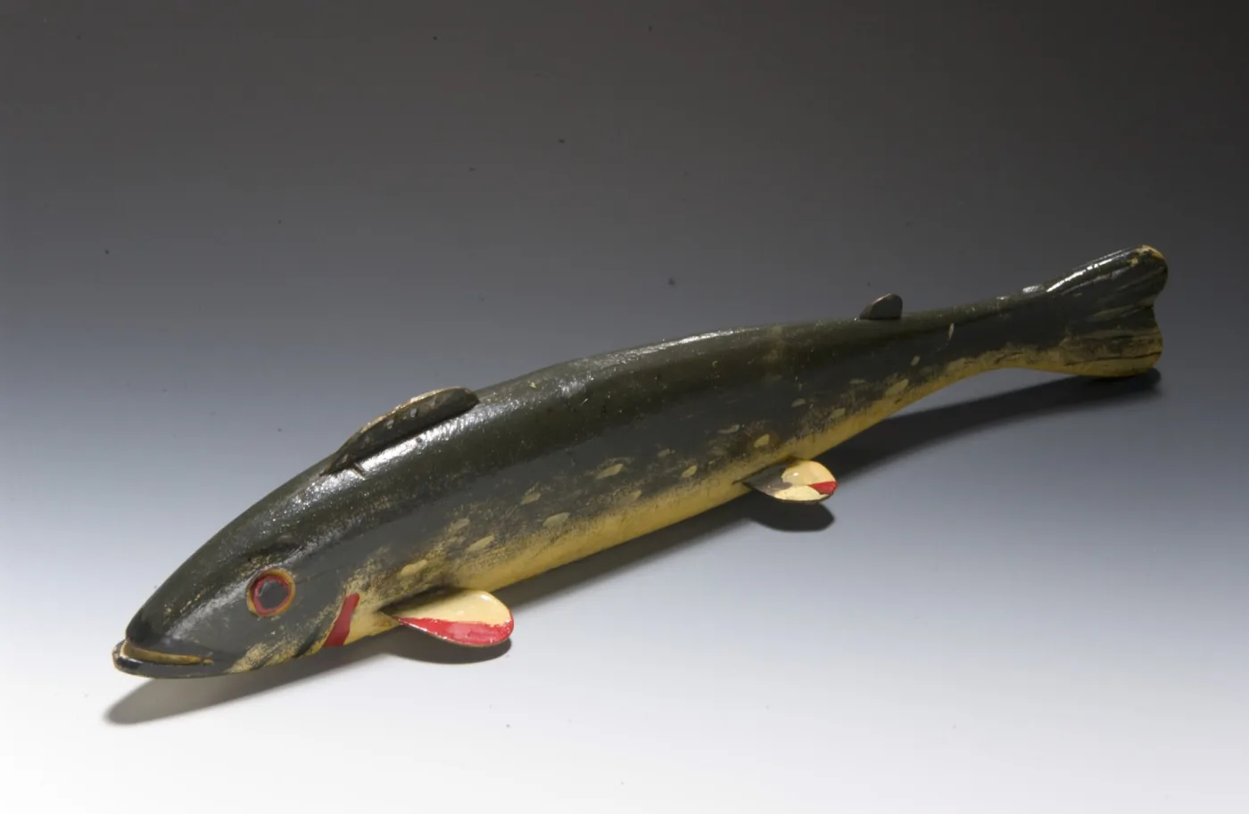 Carved fish decoy painted dark green with yellow spots and red-and-cream tin fins, with a tack eye