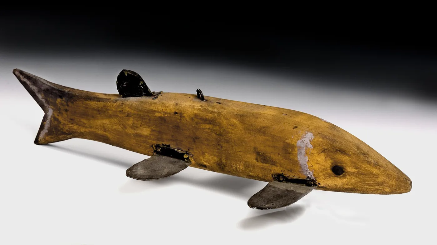 Plain yellow-brown carved fish decoy with dark tin fins screwed to the body and a wire line eye on the back
