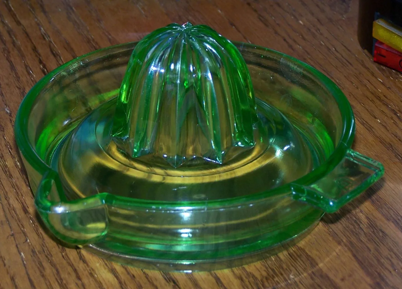 Deep green glass lemon reamer: a ribbed cone rising from a spouted, handled bowl, standing on a wooden table