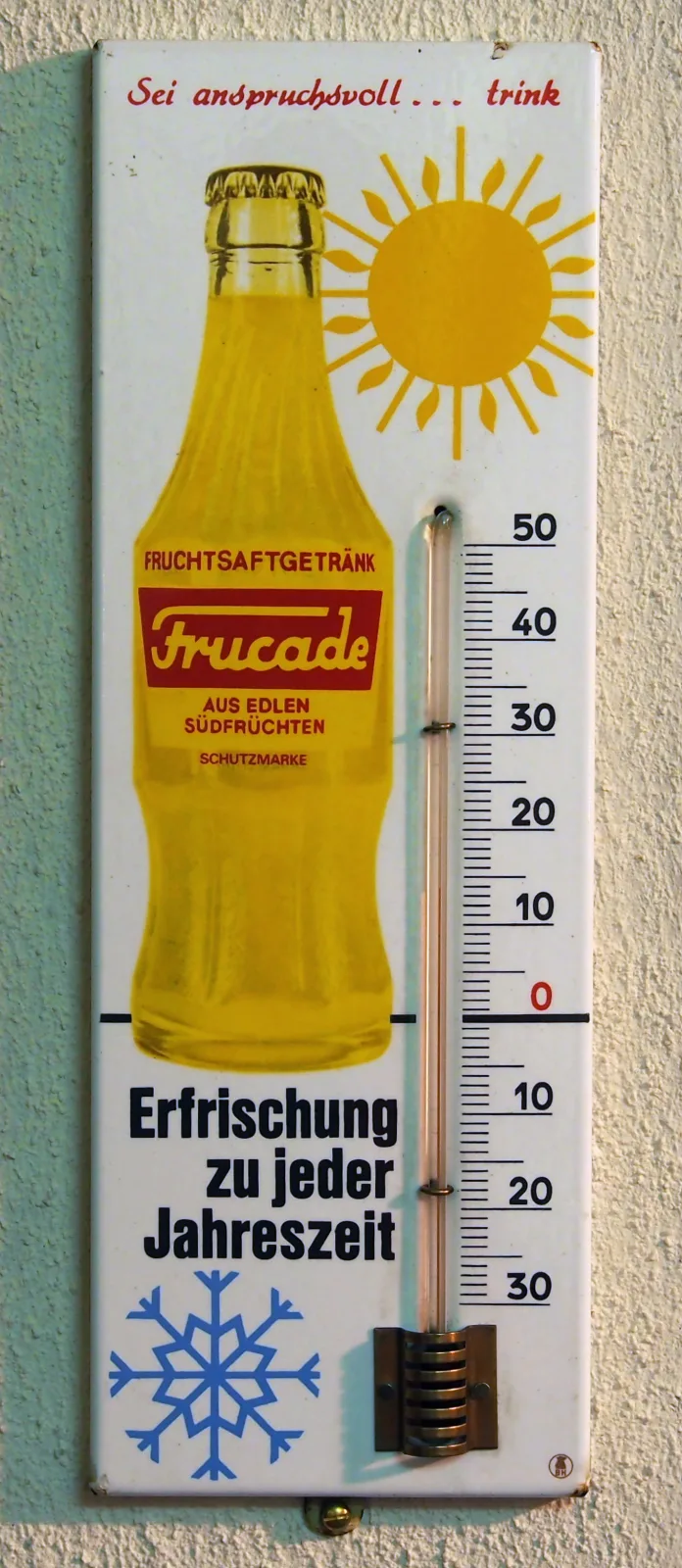 Tall narrow enamel advertising thermometer for Frucade, a yellow bottle and a sun above and a blue snowflake below, with a glass thermometer tube held against the enamel by three metal clips beside a printed centigrade scale